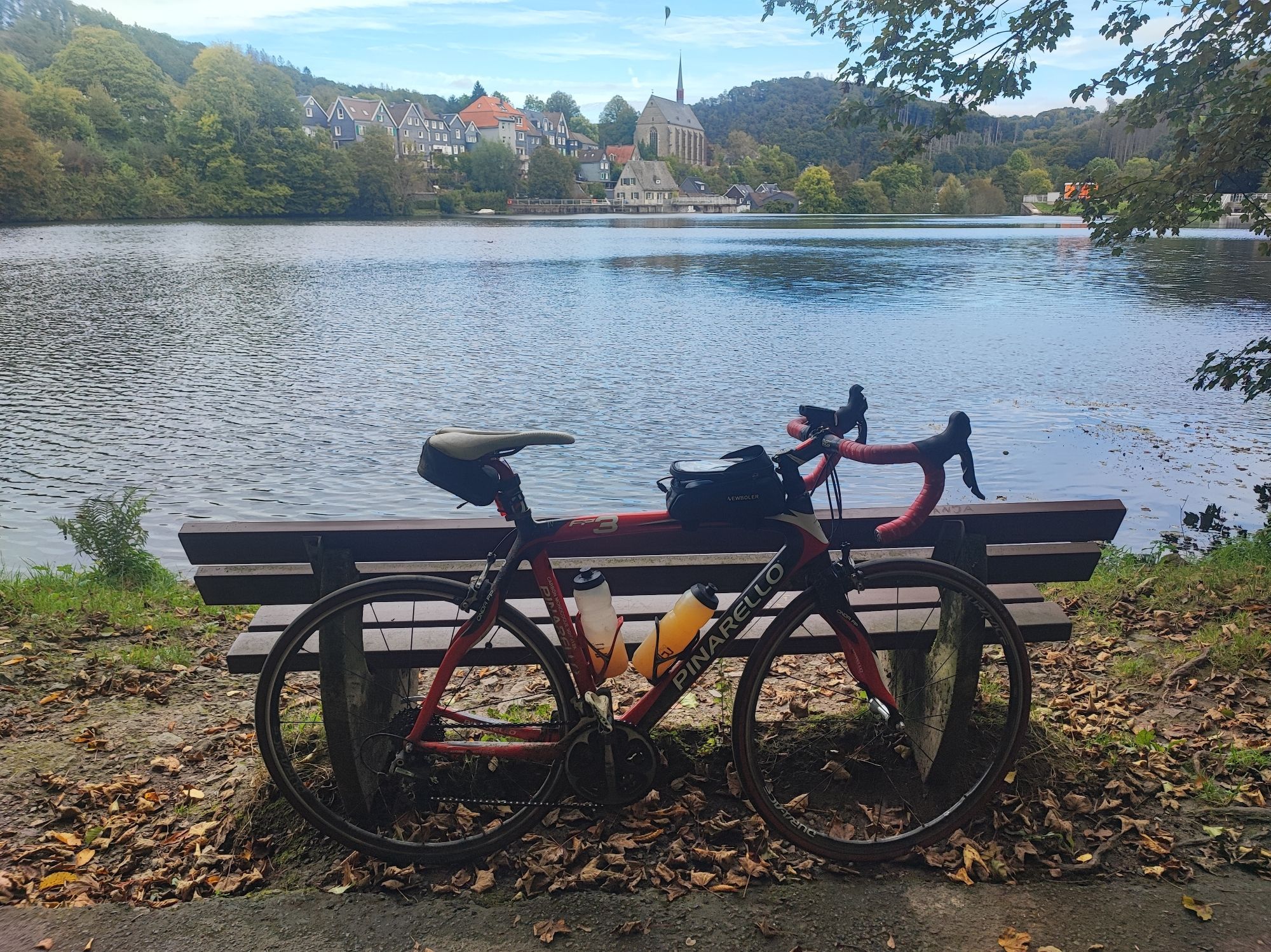 Mein Schwarze-rotes Pinarello Rennrad am Beyenburger Stausee. Im Hintergrund ist das Zentrum von Wuppertal Beyenburg mit in der Mitte eine Kirche zu sehen.