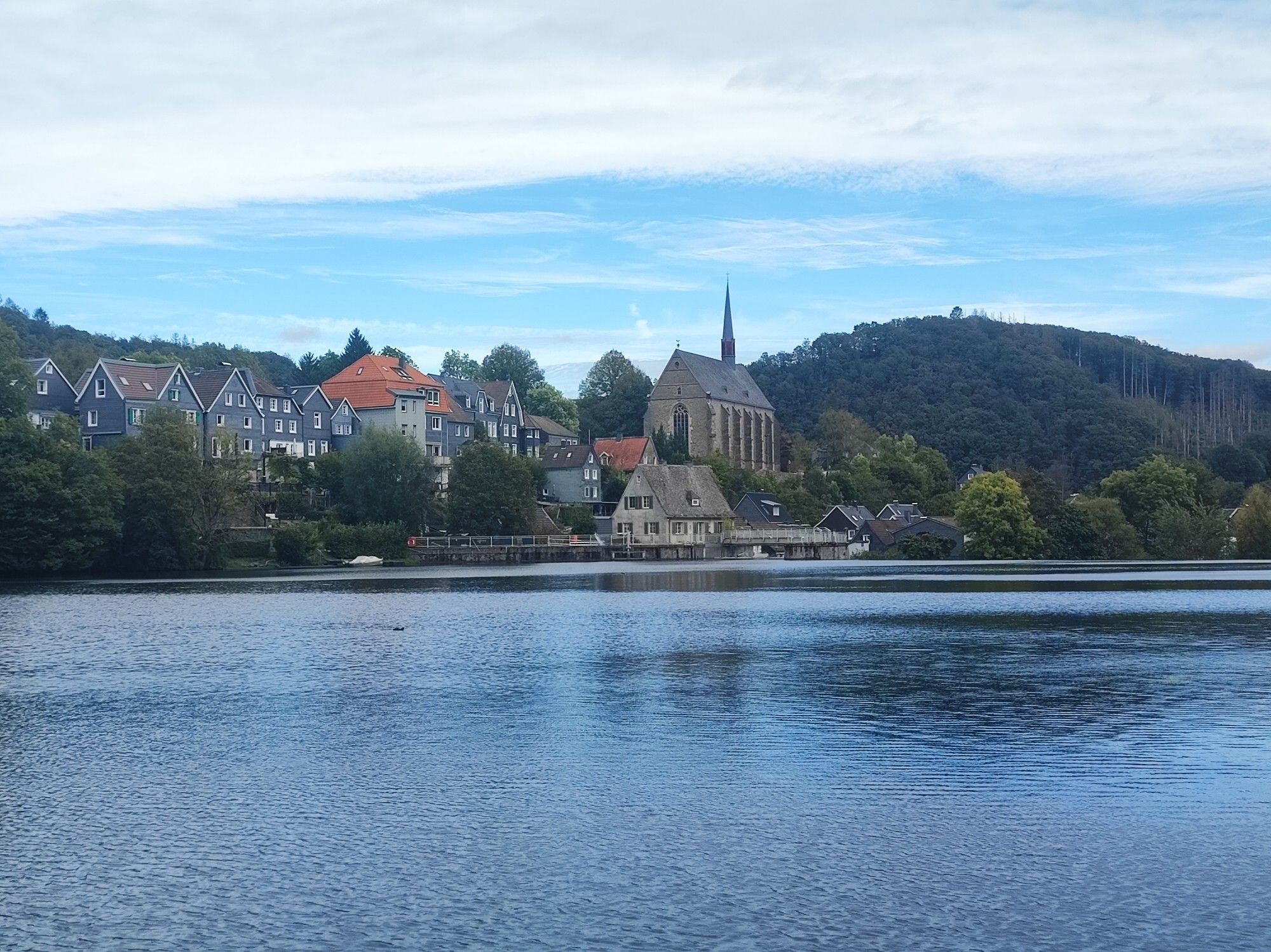 Der Beyenburger Stausee mit in der Mitte der Ortskern von Wuppertal Beyenburg mit einer Kirche. Im Hintergrund ist ein bewaldeten Berg zu sehen.