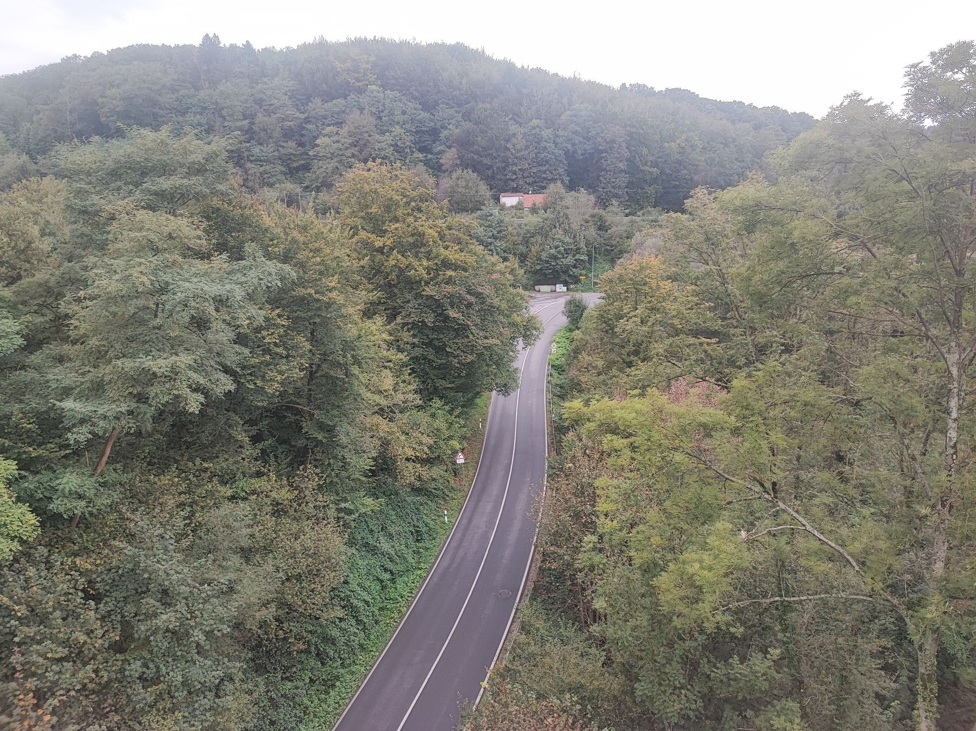 Aussicht vom Panorama Radweg zwischen Essen und Heiligenhaus. Links und Rechts sind Bäume zu sehen. In der Mitte unten eine Straße. Im Hintergrund ein bewaldeten Berg.