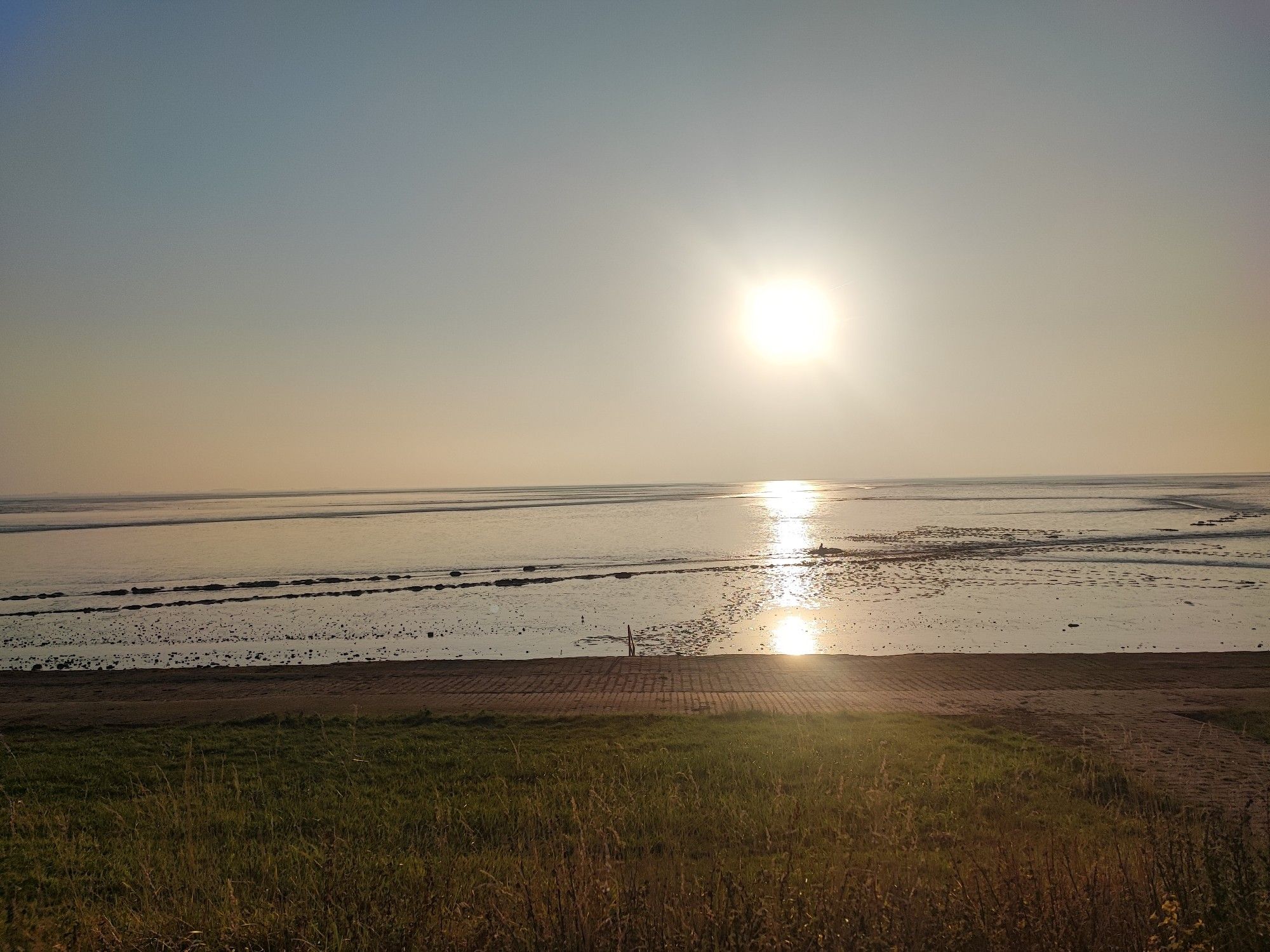 Die Sonne scheint über der Dollart in Ostfriesland. Im Vordergrund ist der Deich zu sehen.