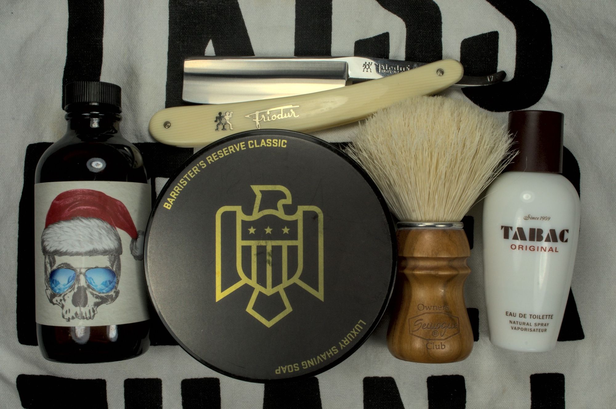 A tub of BaM Reserve Classic with a bottle of BaM Beaudelaire splash, a bottle of Tabac Original frag, a SOC boar brush and a chonky Frio 17 straight razor