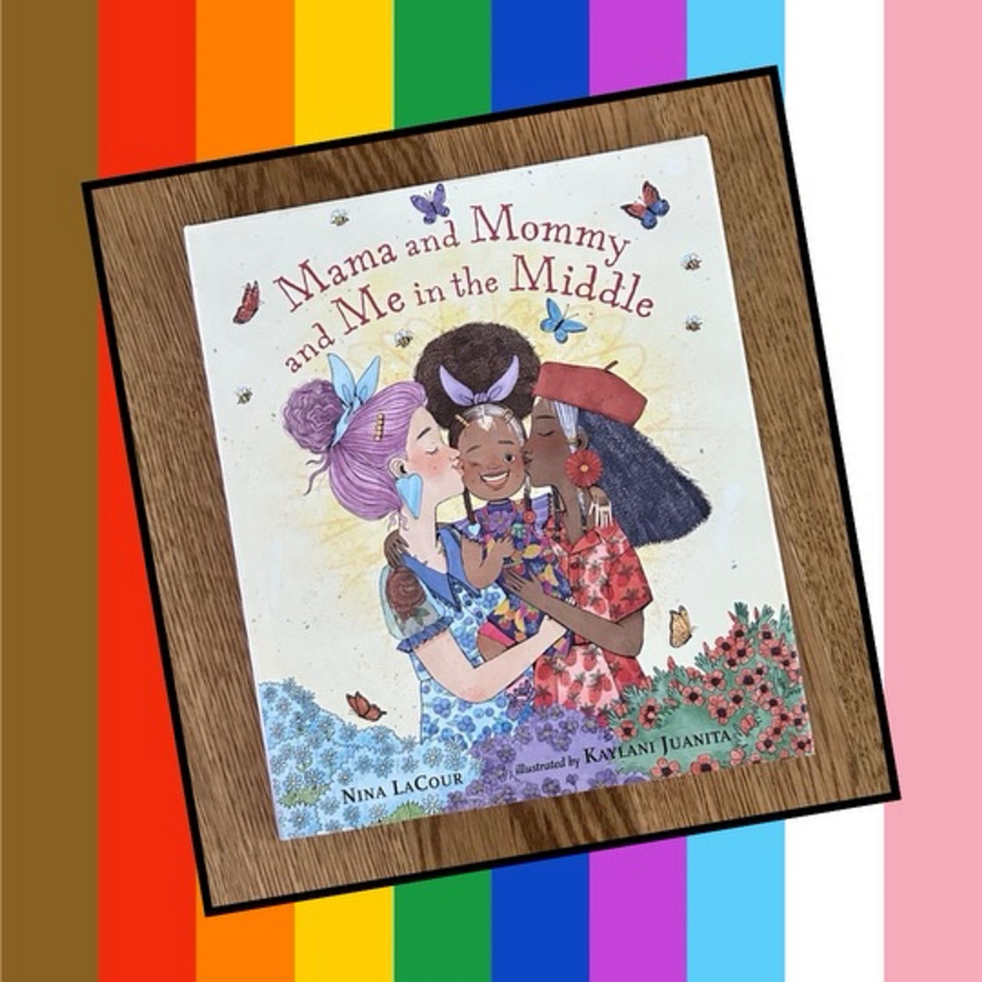 Cover of the picture book Mama and mommy and me in the middle by Nina lacour and Kaylani Jaunita on a rainbow background. The cover shows a child between their two moms getting a kiss on the cheek from each.