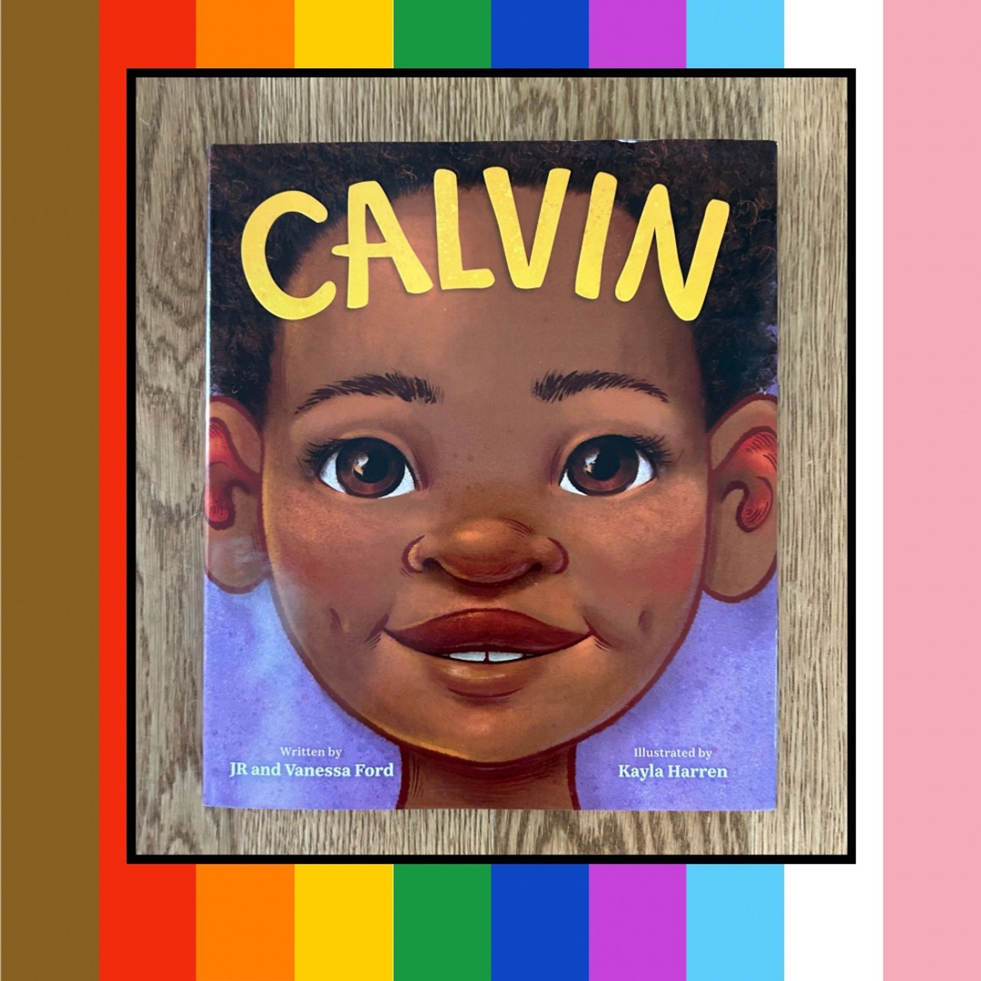 Rainbow striped graphic with a picture of a picture book cover on it. The Picture book is CALVIN written by JR and Vanessa Ford and illustrated by Kayla Harren. The book cover shows a close-up of a child's face with the title across his forehead.