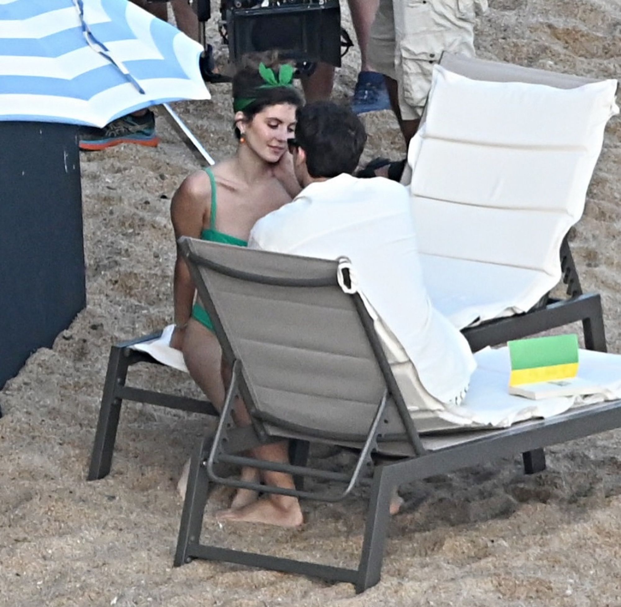 Imagem de Emily Bader e Tom Blyth sentados em cadeiras reclináveis na praia. Eles estão próximos olhando um para o outro.