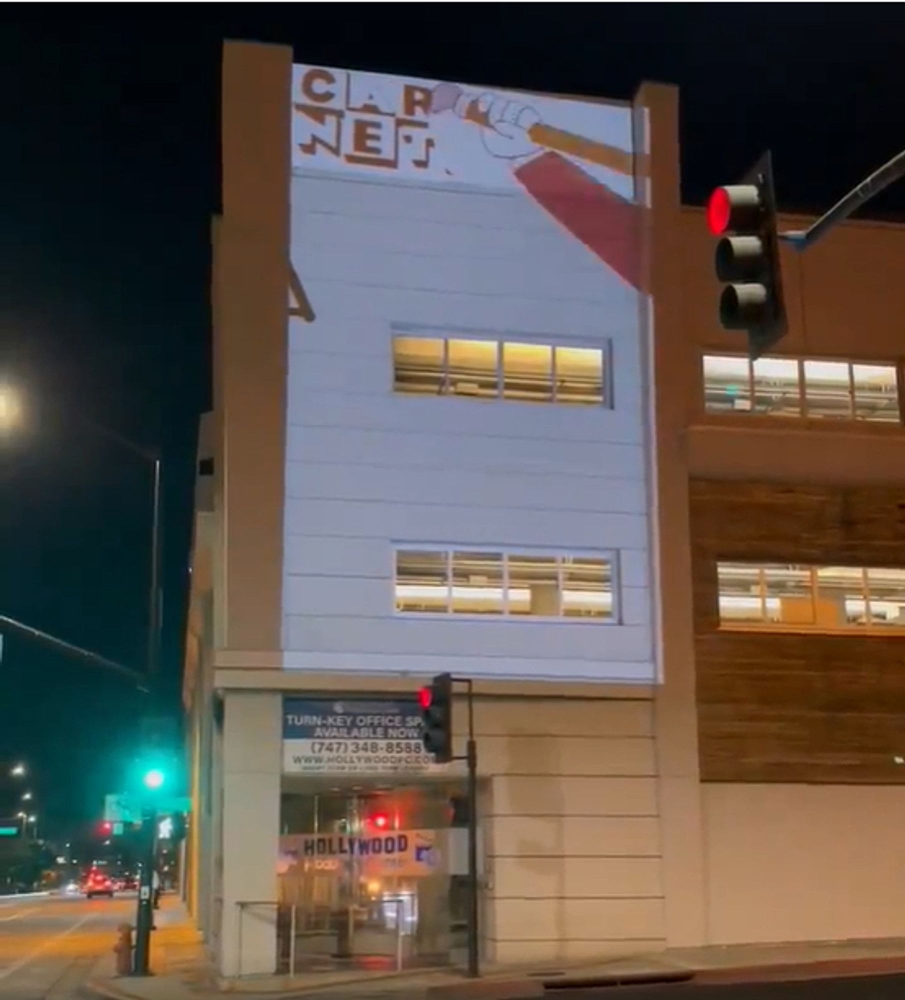 Photo of a building in downtown Burbank at night. An animated clip is projected on the side of the building. A cartoon hand holding a pencil, eraser end down, erases the classic Cartoon Network logo at the top of the building.