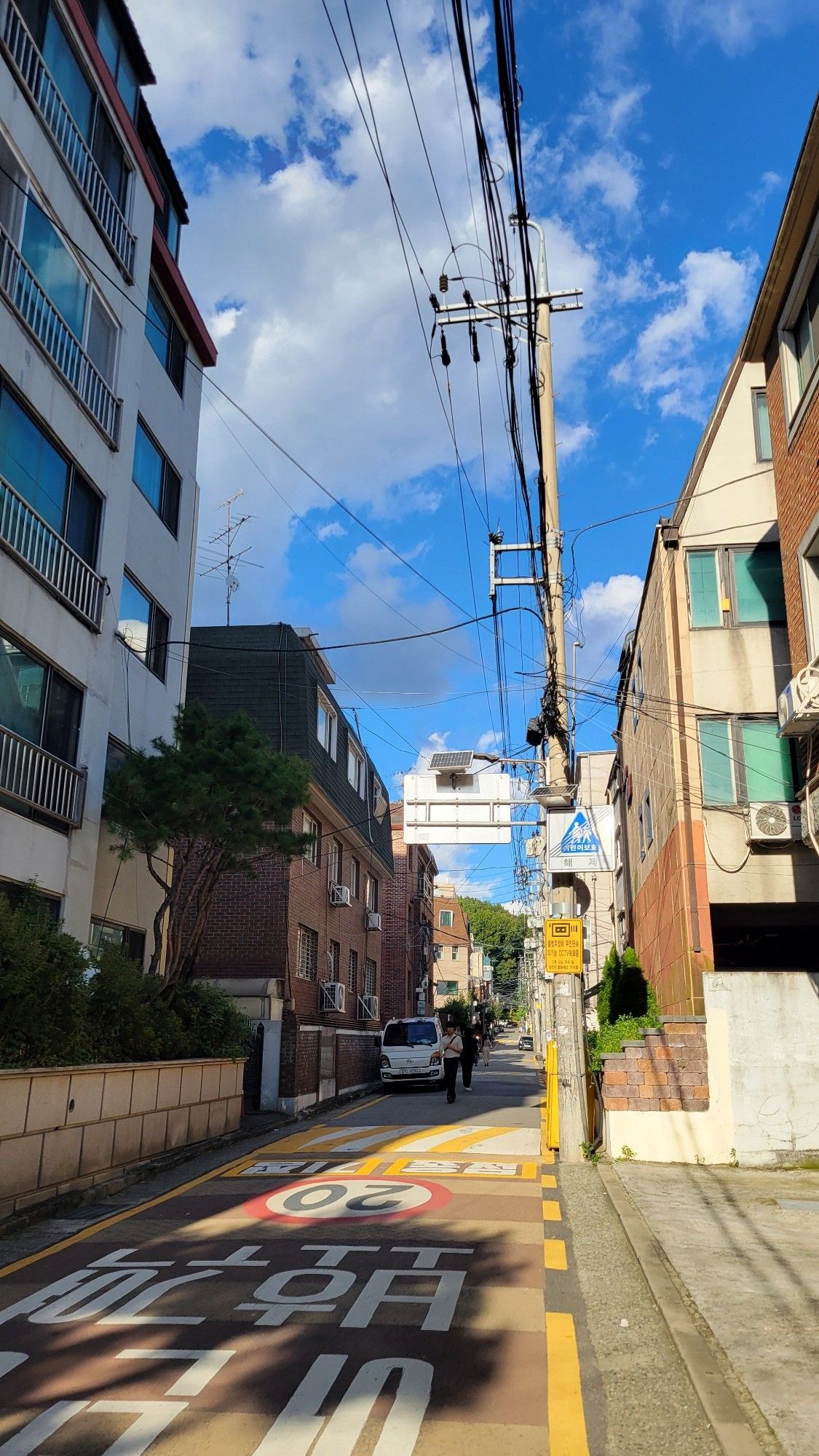 A photo of a street in Korea, the sky is bright blue with a scattered clouds and the lighting is orange with an early sunset glow.