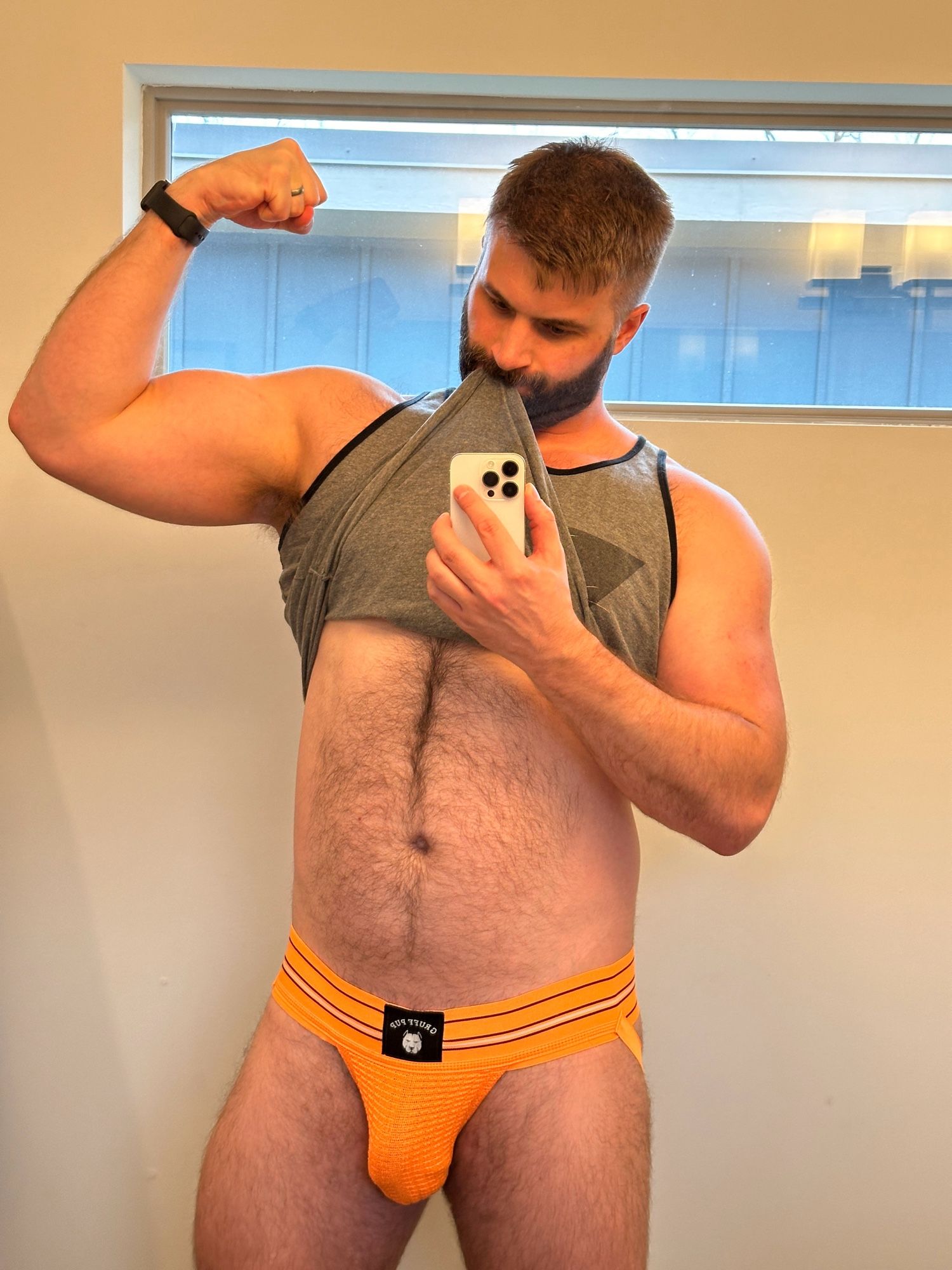 Flexing in the mirror. Wearing an orange jockstrap.