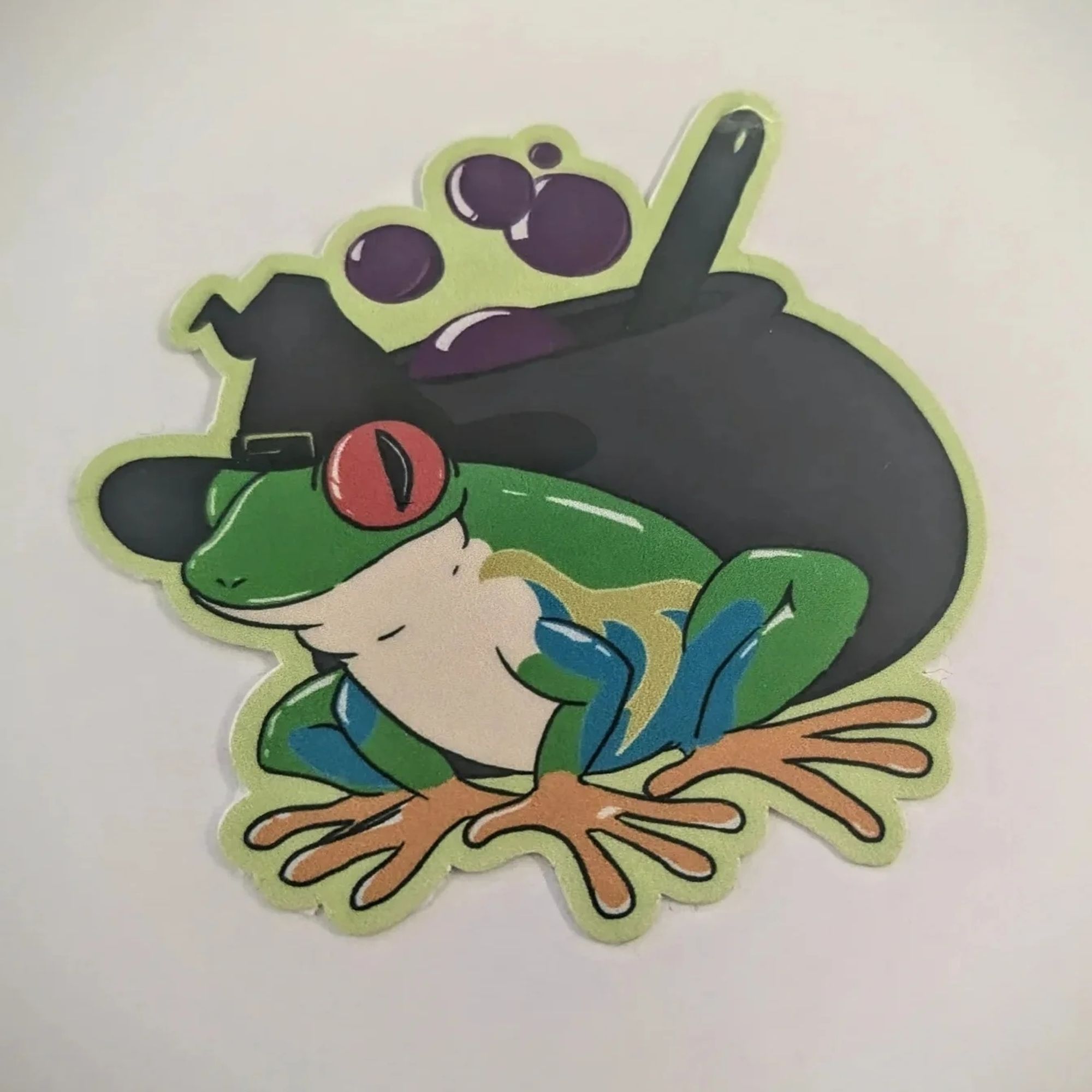 A red-eyed tree frog dressed in a witch's hat in front of a bubbling cauldron