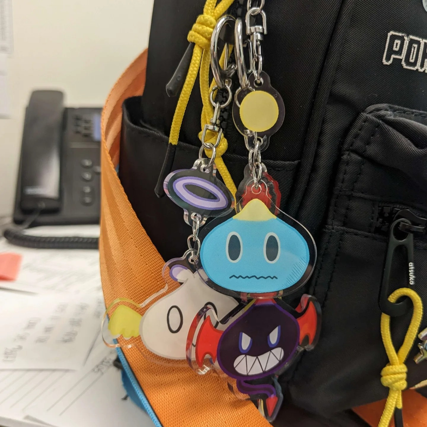 A photo of a bag featuring keychains of the Neutral Chao, Dark Chao, and Hero Chao from the Sonic the Hedgehog series