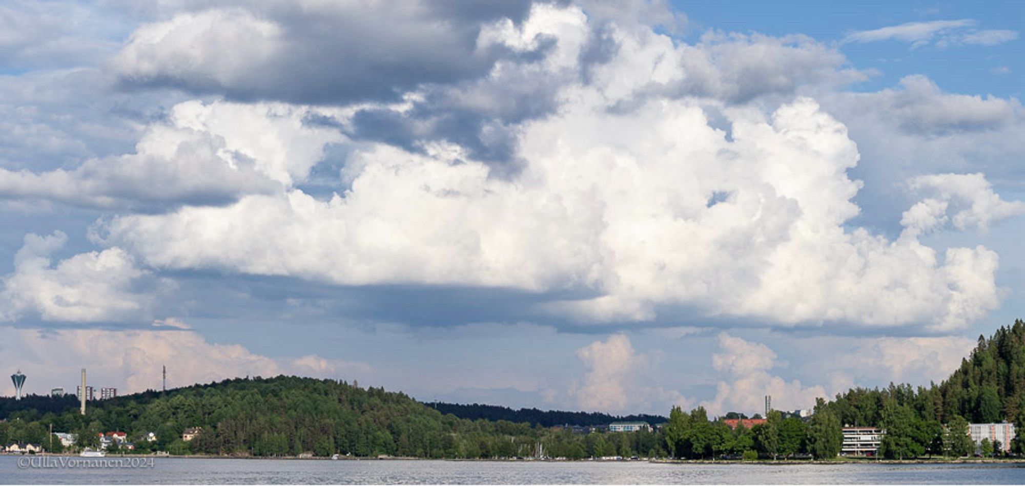 Maisemakuva järven yli. Maiseman yllä isot muhkeat kumpupilvet.