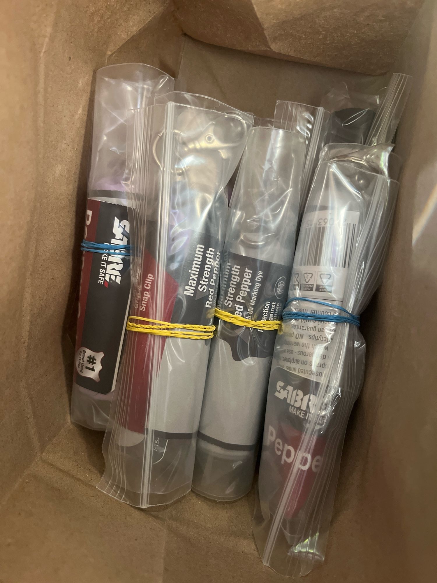 Image shows a dozen pepper gel spray units along with instructions on their use individually wrapped in ziplock bags and secured with rubber bands in a brown paper sack. These are then inserted into care packages for distro.