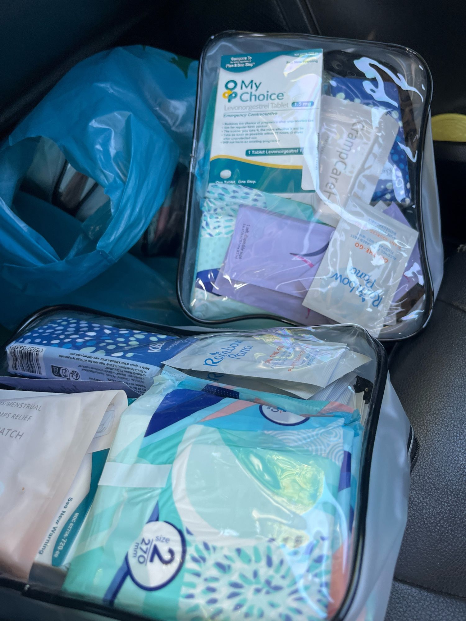 Image shows a dozen clear zippered pouch full of menstrual products, birth control, emergency birth control, chocolates, cramp and pain relief, lube, tissues, body wipes, pepper gel spray and hand sanitizer packed into plastic bags in the floorboard of the Mutual Aid Mobile. These mutual aid packages are distributed regularly and are highly requested from our community.