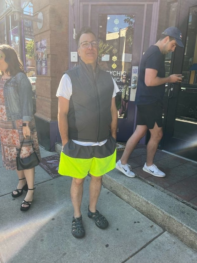 Picture of a man in Florescent shorts, white shirt and grey vest.