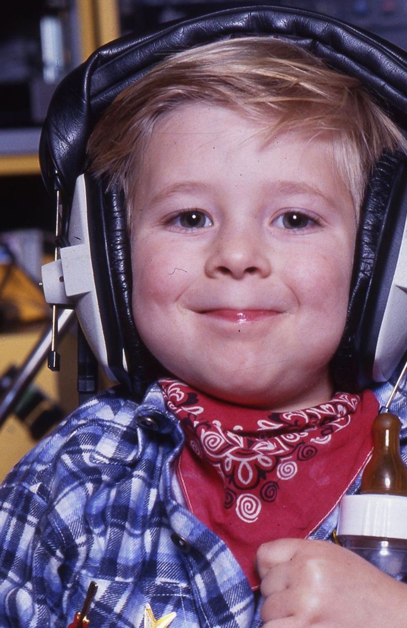 Photo de Jordy à 4 ans, le fameux crooner parolier, à l'origine du tube intergénérationnel "Dur dur d'être bébé".
Il porte un casque audio sur les oreilles et un bandana rouge autour du cou.