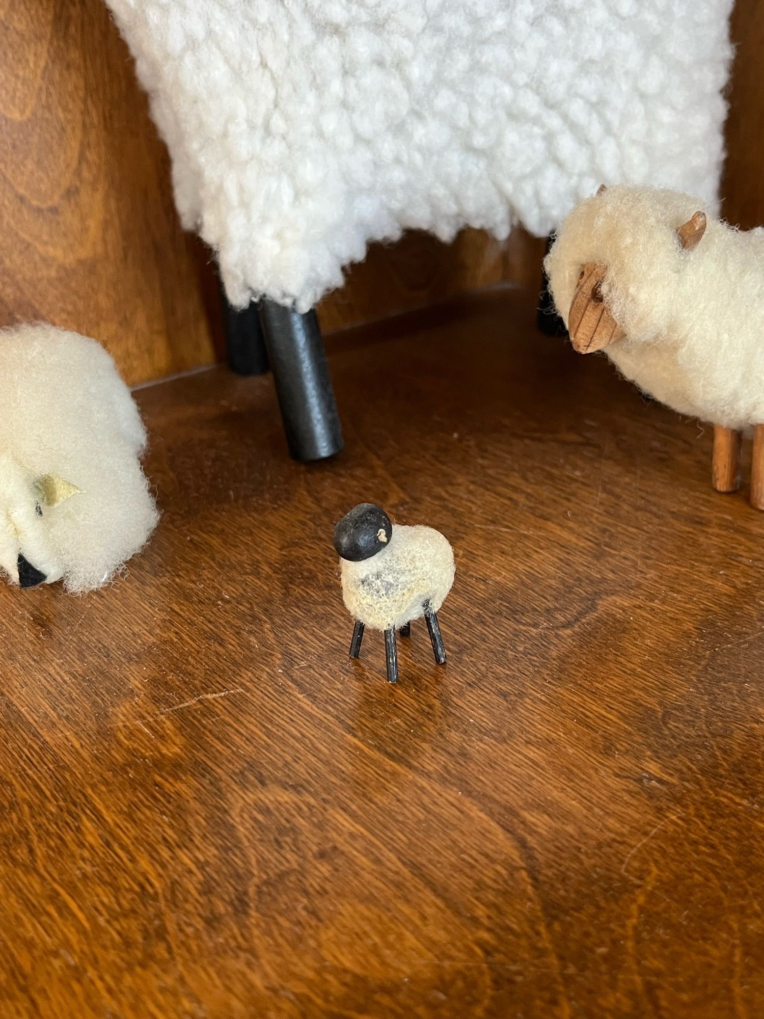 the smallest ever figure of a sheep, surrounded by slightly larger figures of sheep. all have wood bodies with real wool fur.