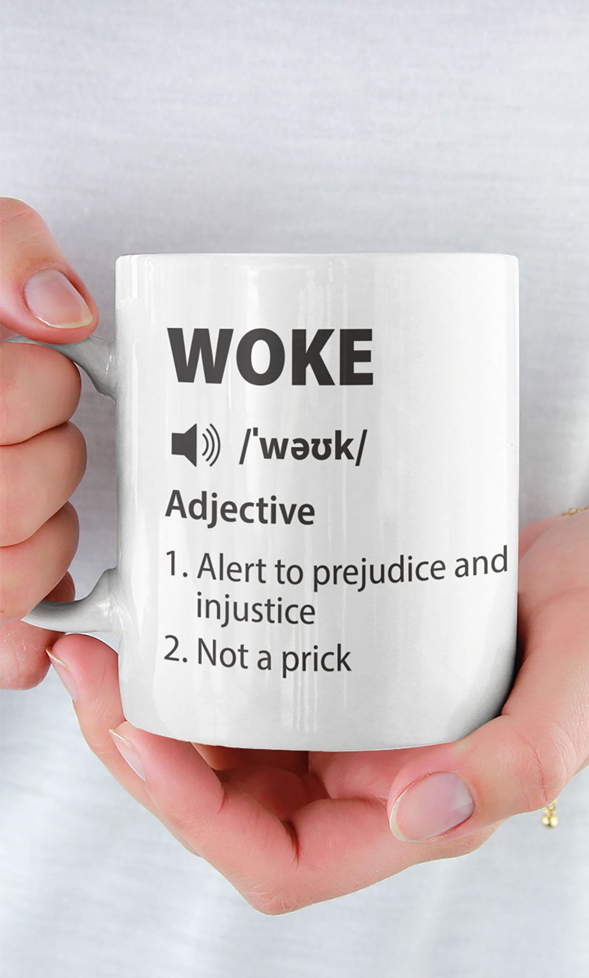 A woman holding a white mug with a definition of "Woke", saying "Alert to prejudice and injustice" and "Not a prick"