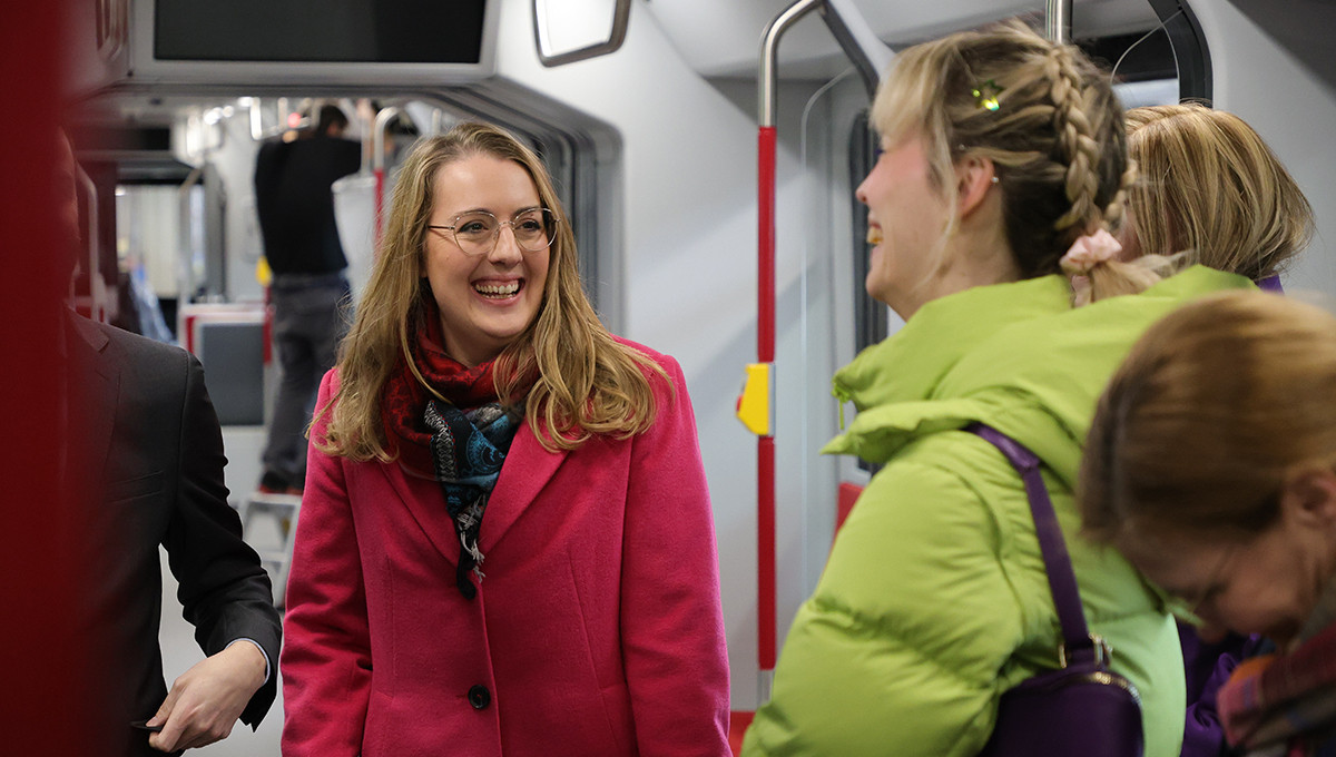 Die Fraktionsvorsitzende Katharina Dröge und mehrere Grüne Bundestagsabgeordnete stehen in einer Straßenbahn und unterhalten sich.