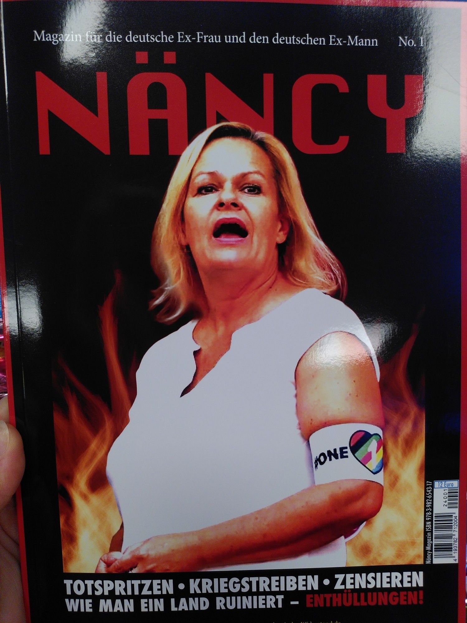 Das Cover der Zeitung "Näncy".
Abgebildet ist Nancy Faser im weißen Top und Regenbogenarmbinde; hinter ihr schlagen Flammen hoch.
Text:Magazin für die deutsche Ex-Frau und den deutschen Ex-Mann. No 1.
TOTSPEITZEN-KRIEGSTREIBEN-ZENSIEREN
WIE MAN EIN LAND RUINIERT -- ENTHÜLLUNGEN!