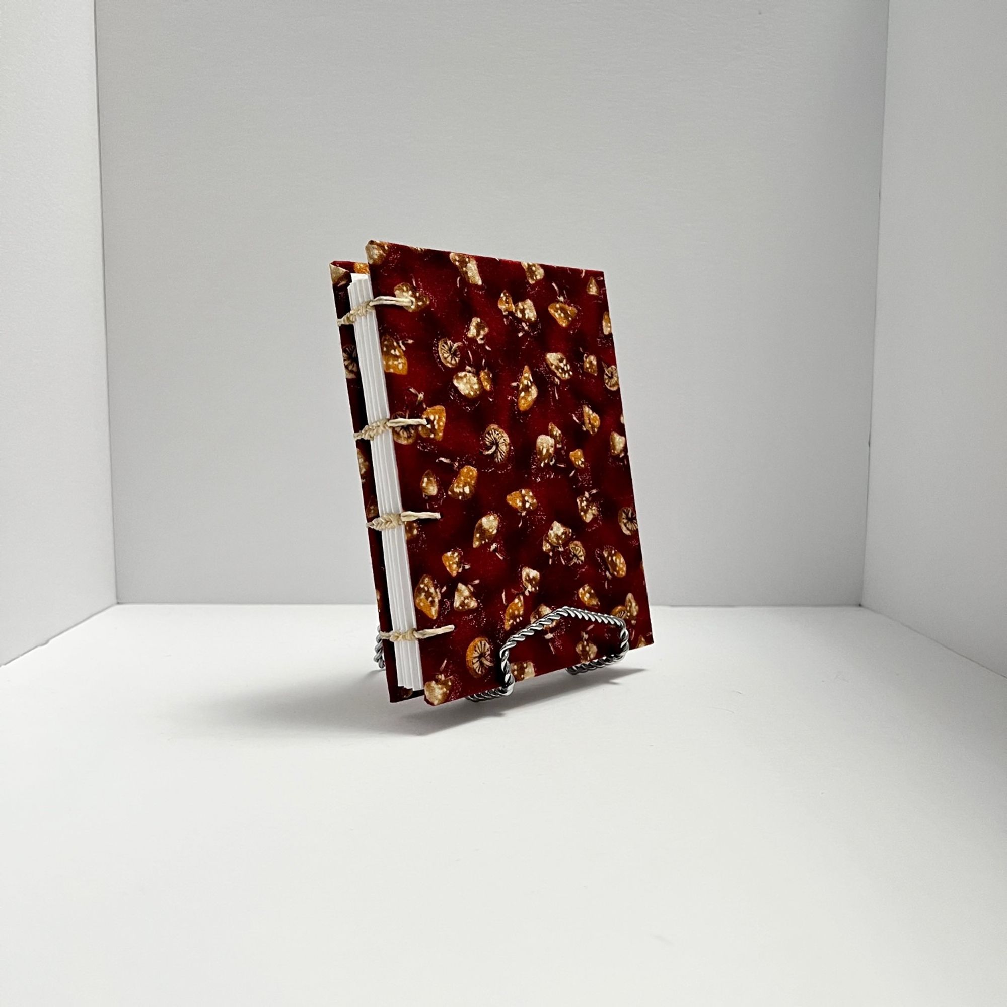 a hand bound coptic stitch journal with mushroom patterned red and brown covers.