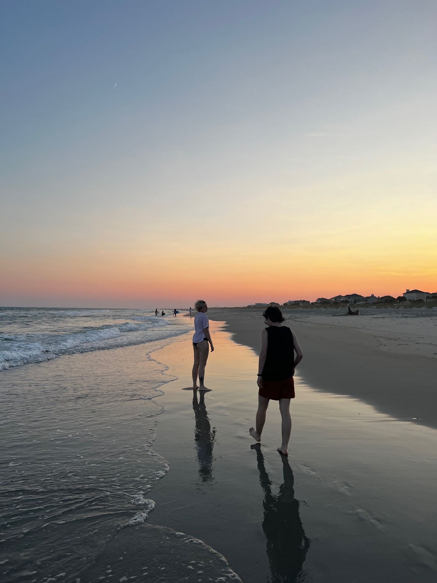 two people walking along the beach at sunset