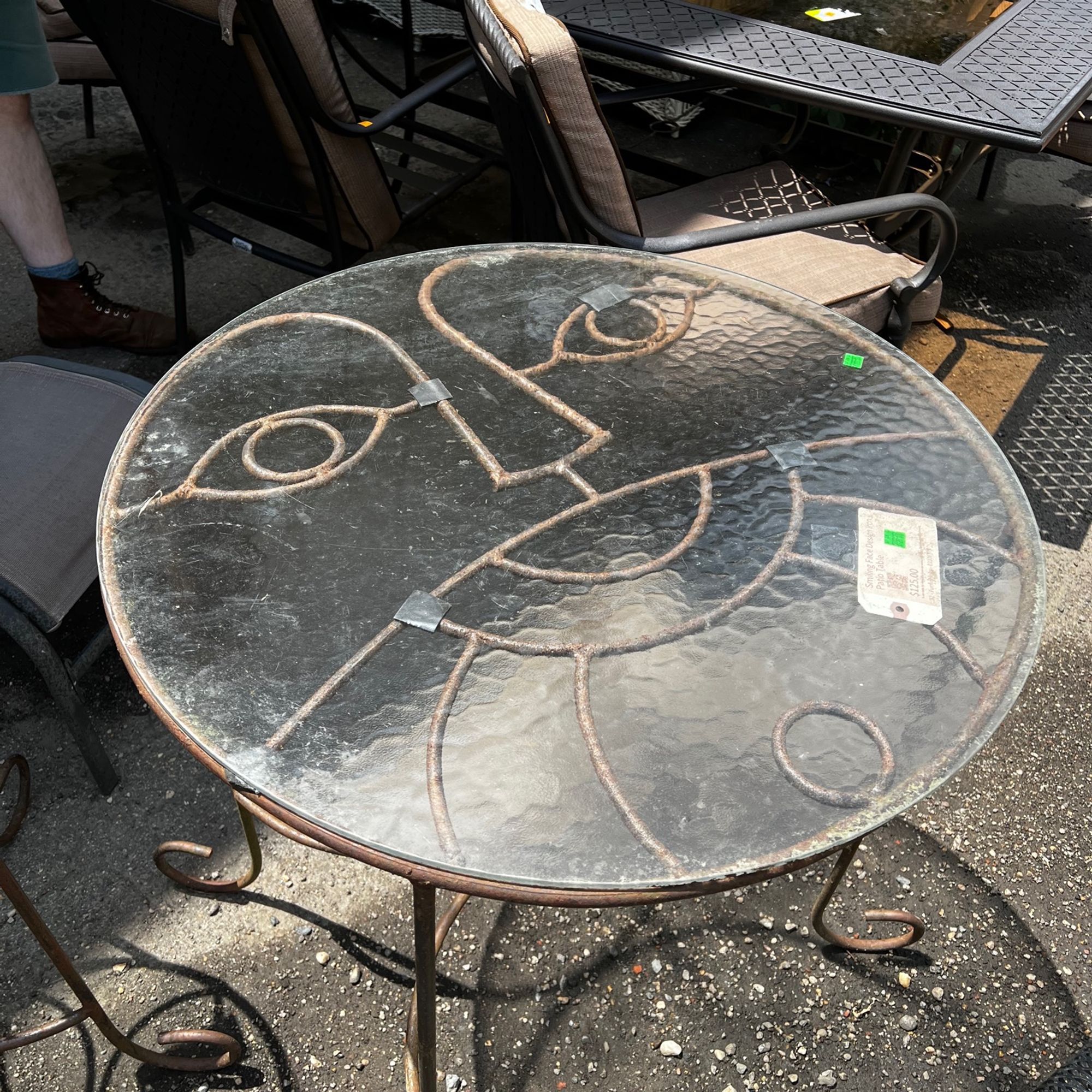 photo of a glass top outdoor table with a happy face design make out of the iron support, visible through the glass