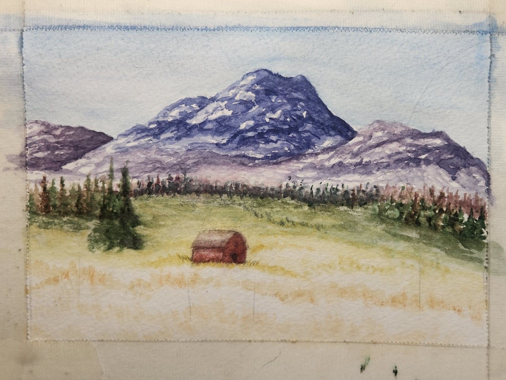 A watercolour lanscape painting of a barn nestled in the foothills amid grasses and conifers. A range of purple mountains in the backgroud.