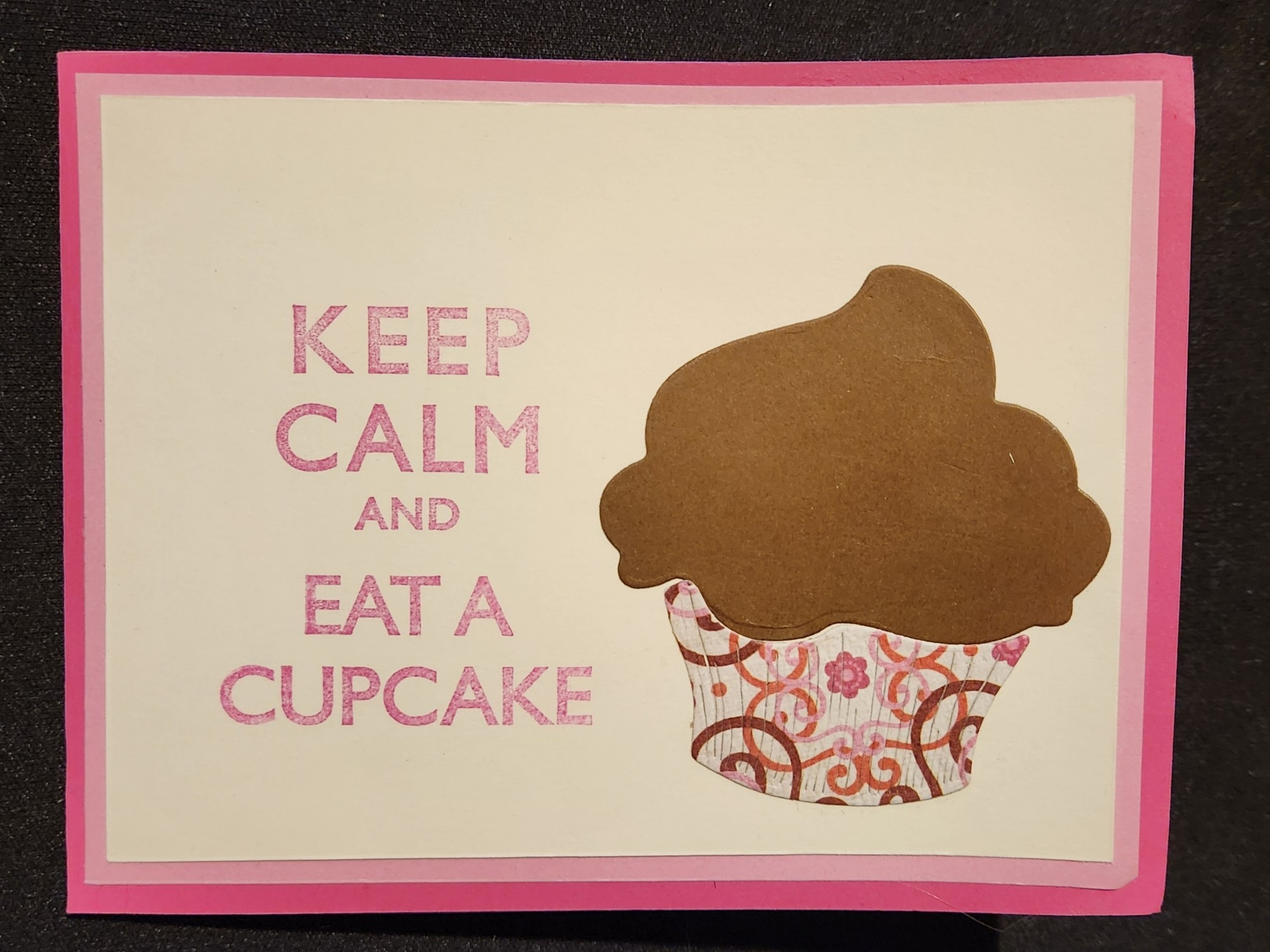 The inside of a handmade card features the saying "Keep calm and eat a cupcake" stamped in hot pink on ivory cardstock. The ivory panel is matted on pale pink.

The brown that is visible through the cutout window is actually chocolate frosting on a diecut cupcake. The cupcake paper liner is diecut from the same brown and pale filigree patterned paper that is used for the front of the card.