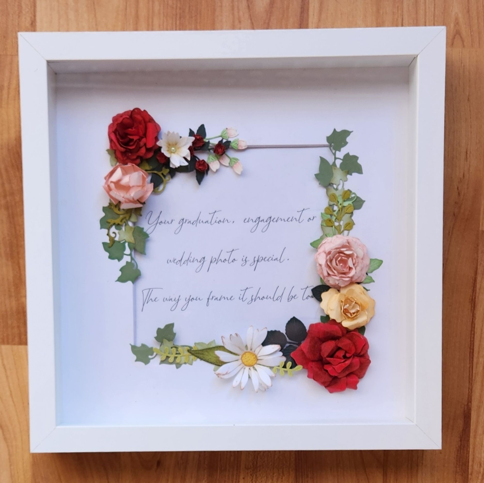 A shadowbox with flowers, including rosds and daisies, handsculpted from paper diecuts