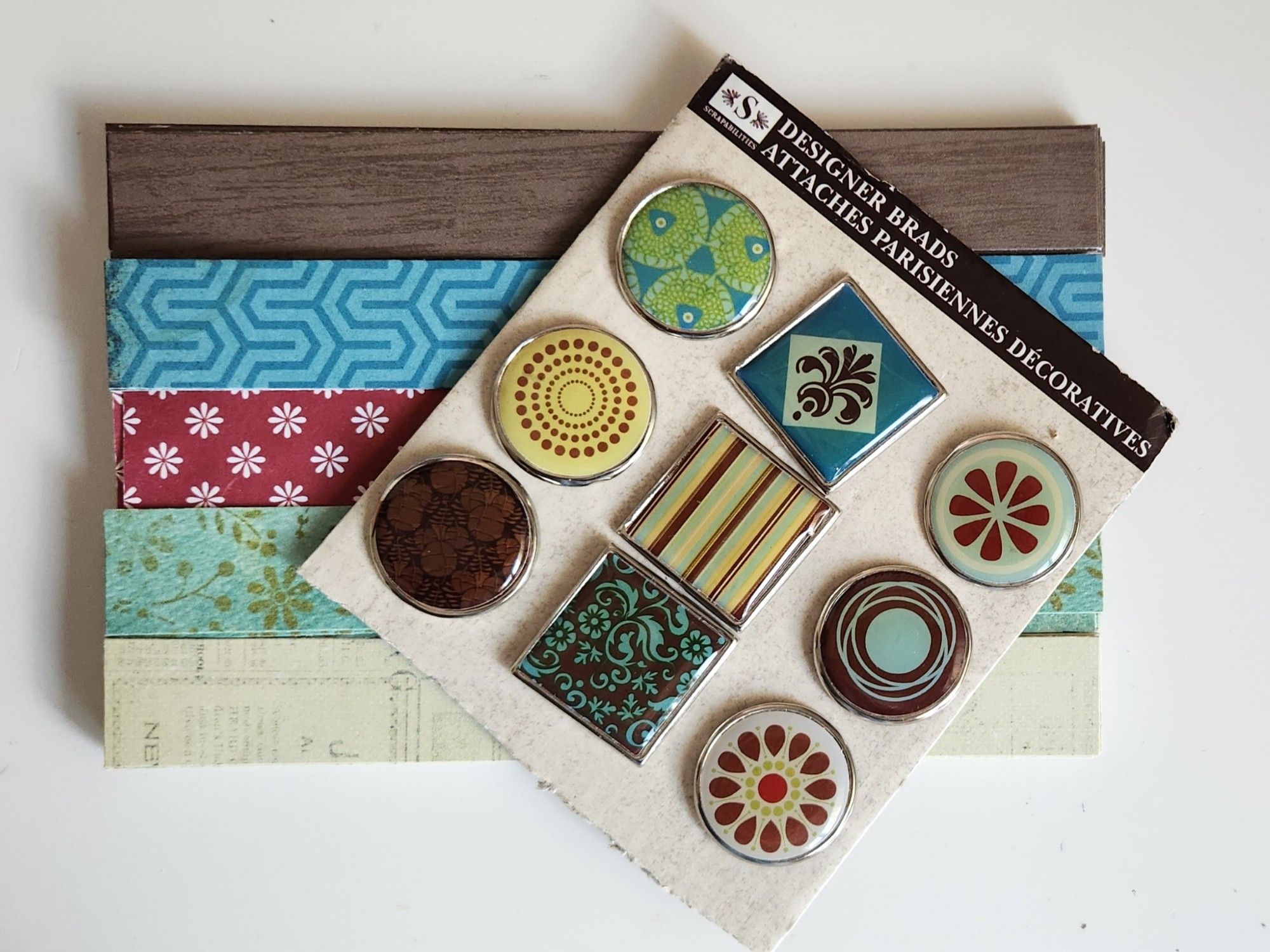 Decorative craft brads and strips of coordinating scrapbook paper in brown, teal blue, deep red, aqua, and yellow-green.