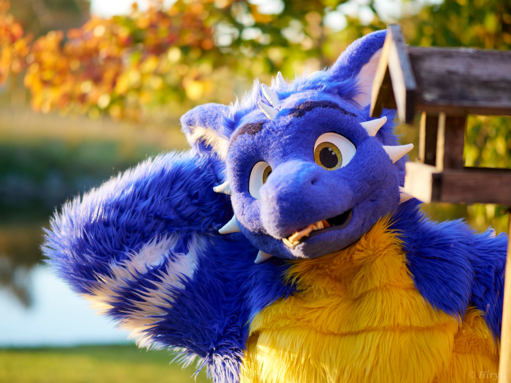 A blue furry dragon standing next to a lake, with the leaves having beautiful autumn colors