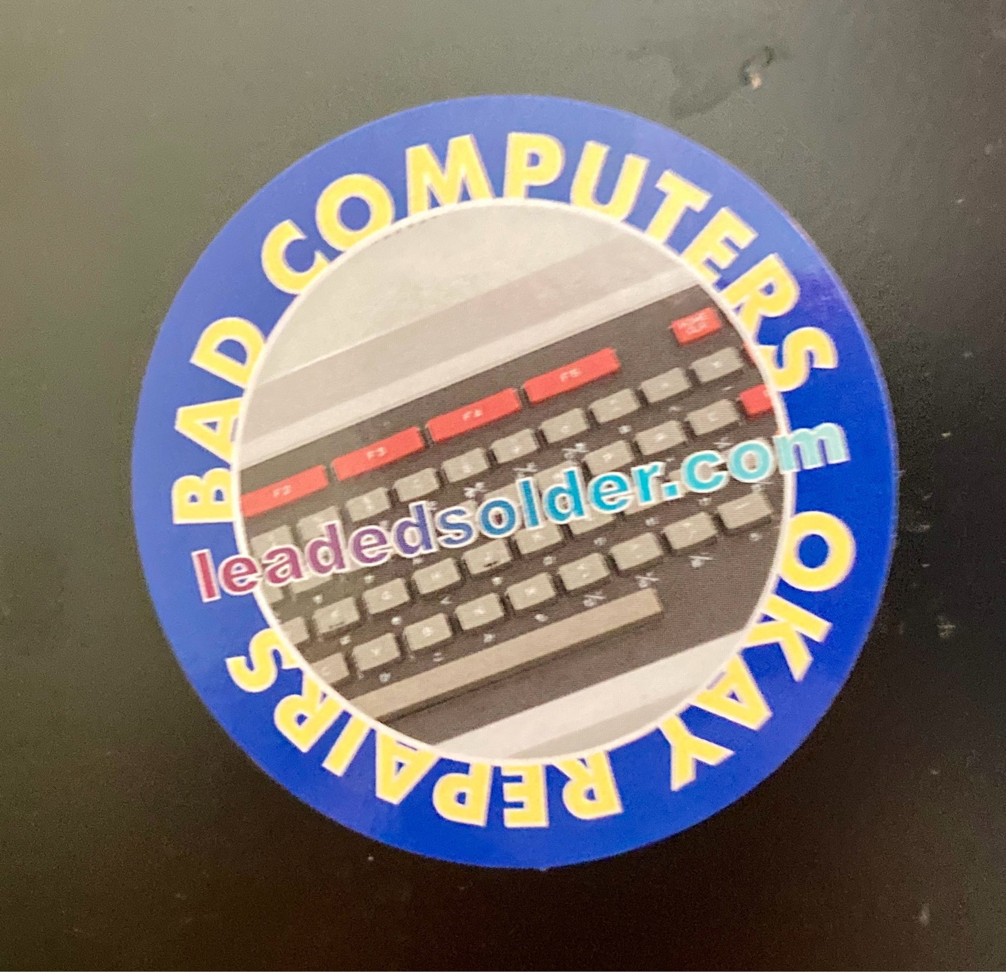 A round sticker saying "bad computers, okay repairs, leadedsolder.com"