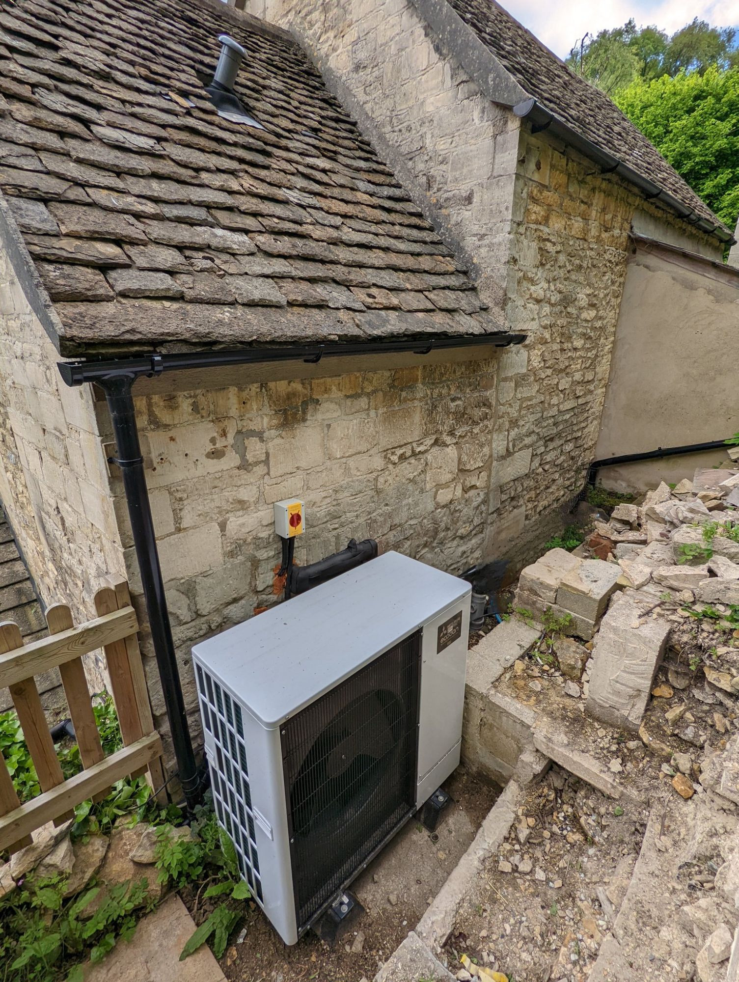 Photo of an old stone building, behind which is a large Mitsubishi heat pump.