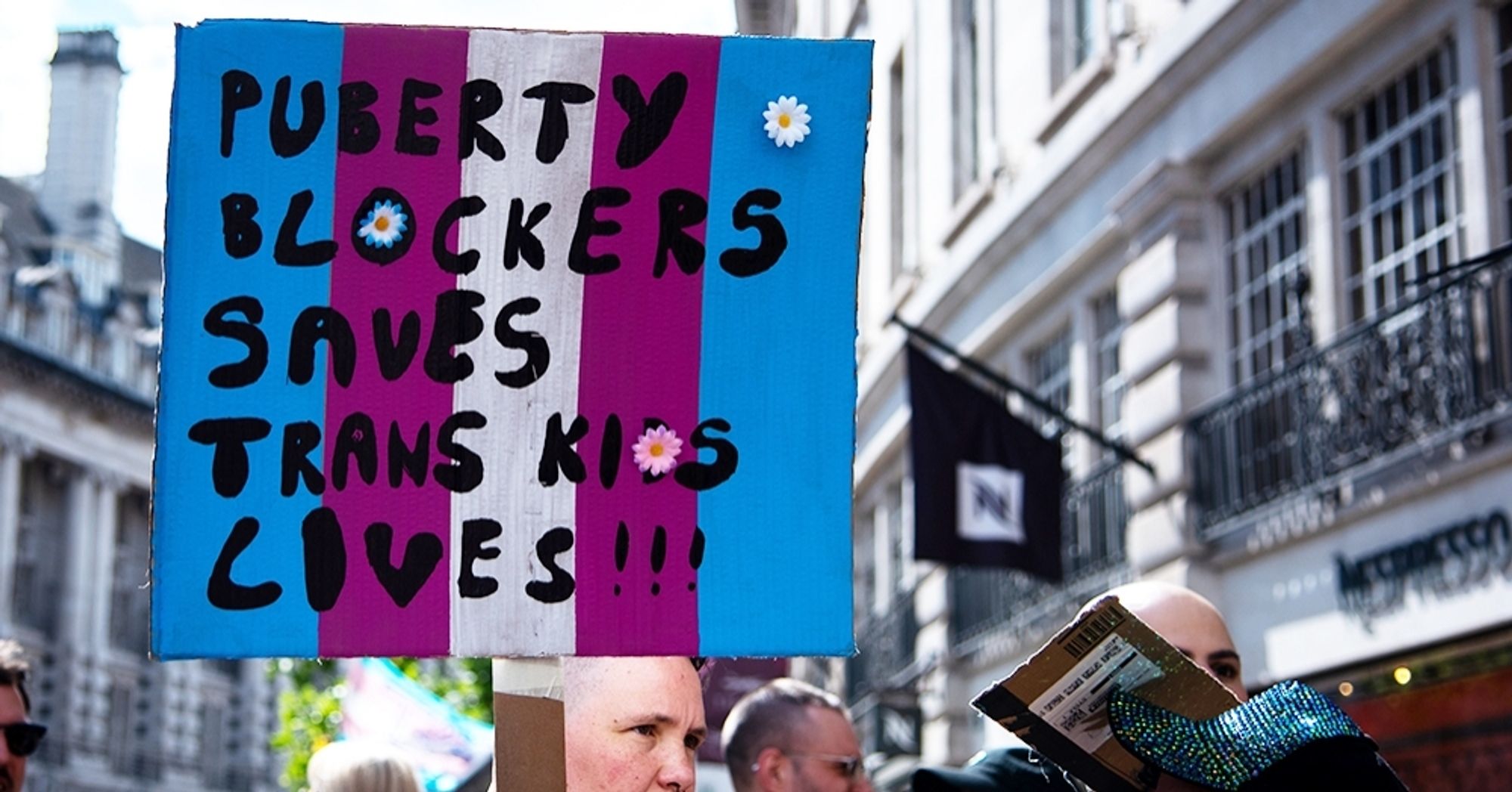 Trans rights campaigners with a sign that reads "Puberty blockers saves trans kids lives!!!"