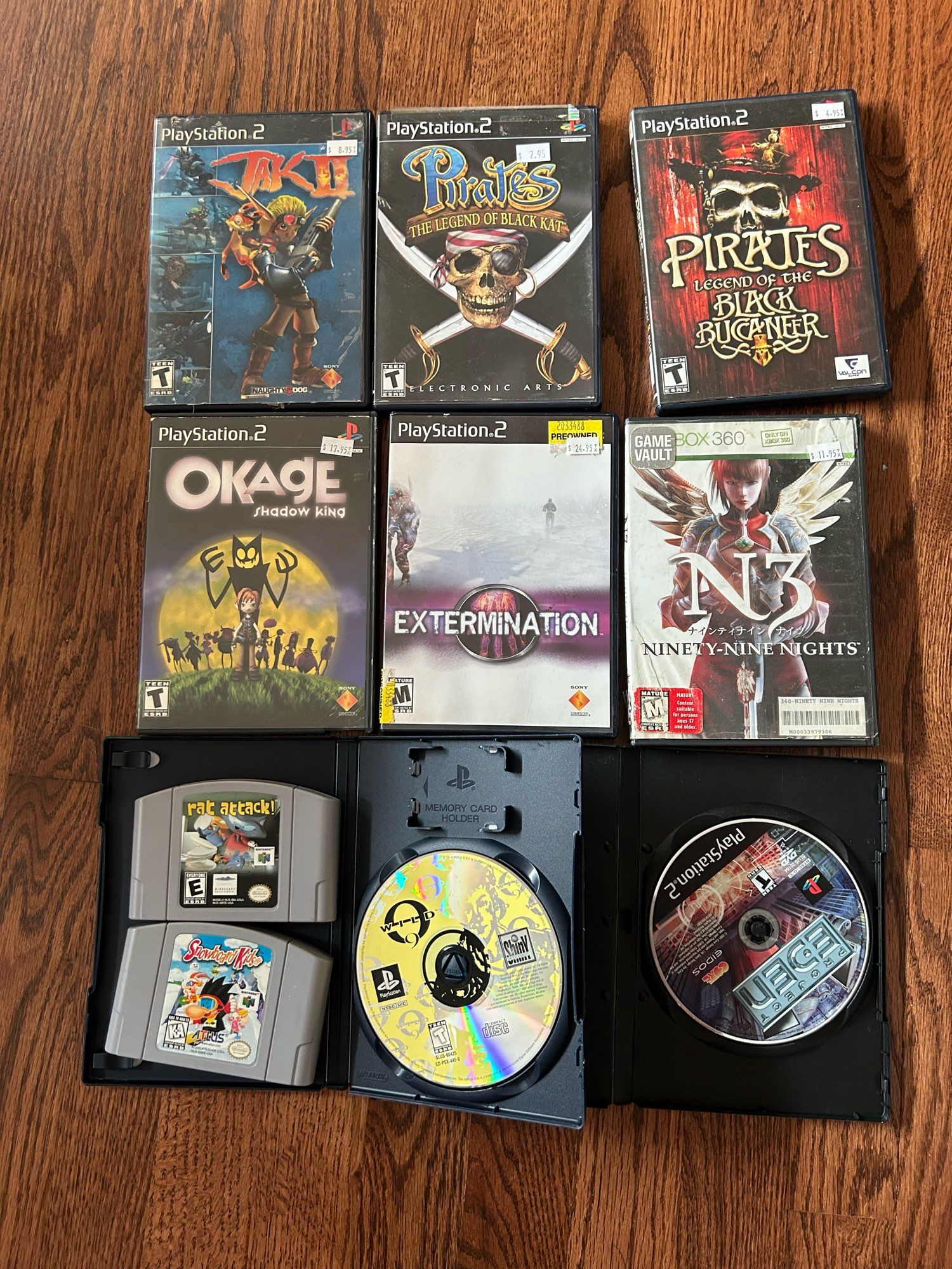 Pile of used video games. Left to right, starting at the top: Jak II, Pirates: The Legend of Black Kat, Pirates: Legend of the Black Bucaneer, Okage, Extermination, N3, Rat Attack, Snowboard Kids, Wild 9, and Project Eden.