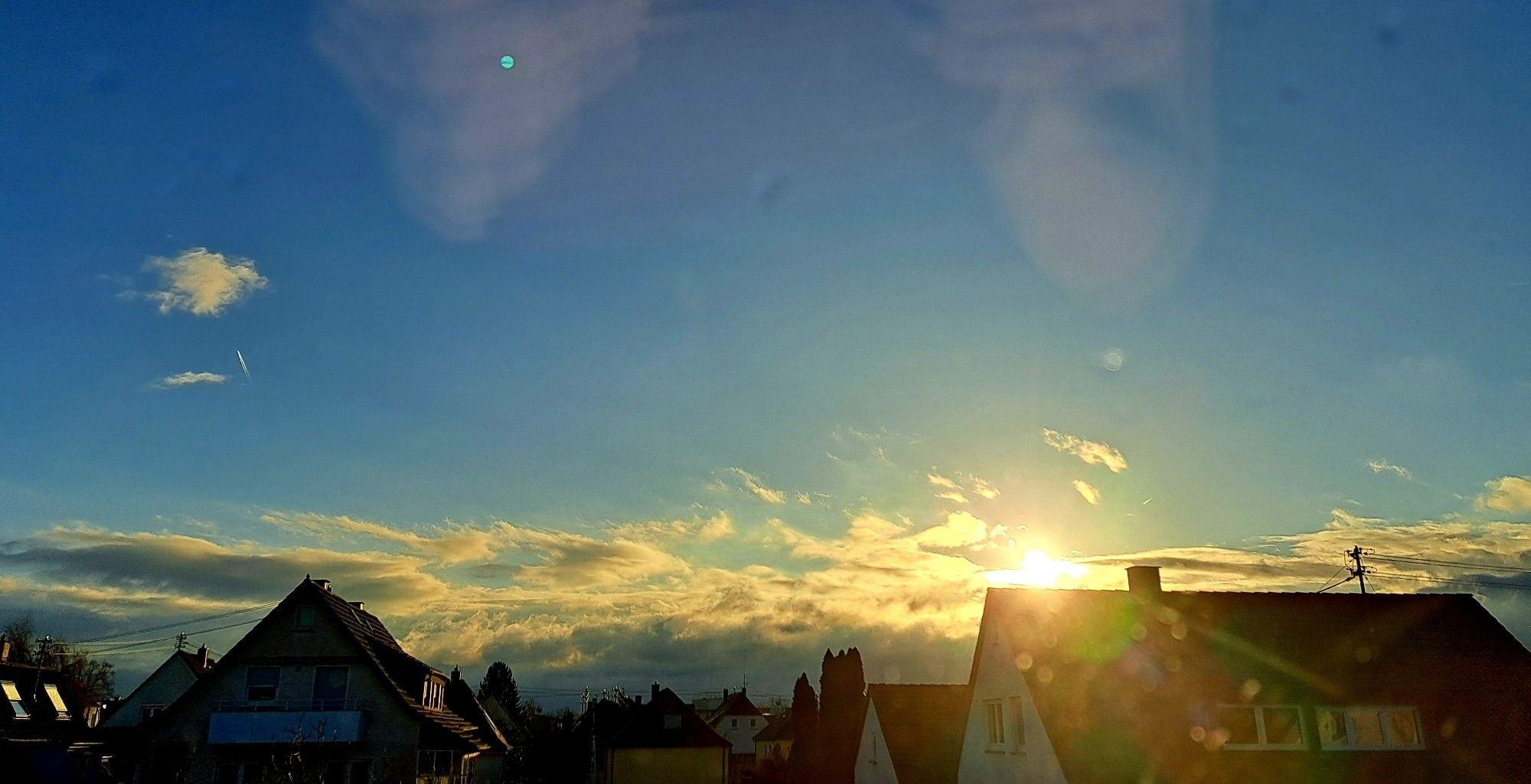 Blick aus dem Dachfenster. Blauer Himmel, Wolken, Gegenlicht, Häuserdächer.