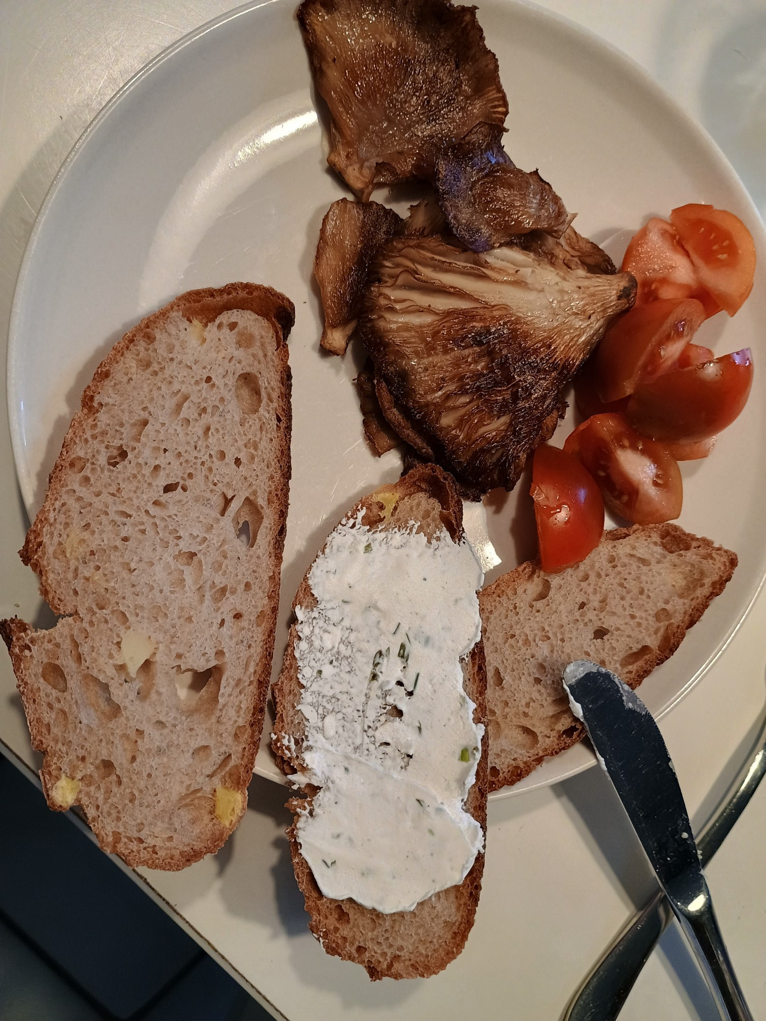 Ein Frühstücktsteller mit Kartoffelbrot, Frischkäse, gebratenen Lungenseitlingen und Tomaten.