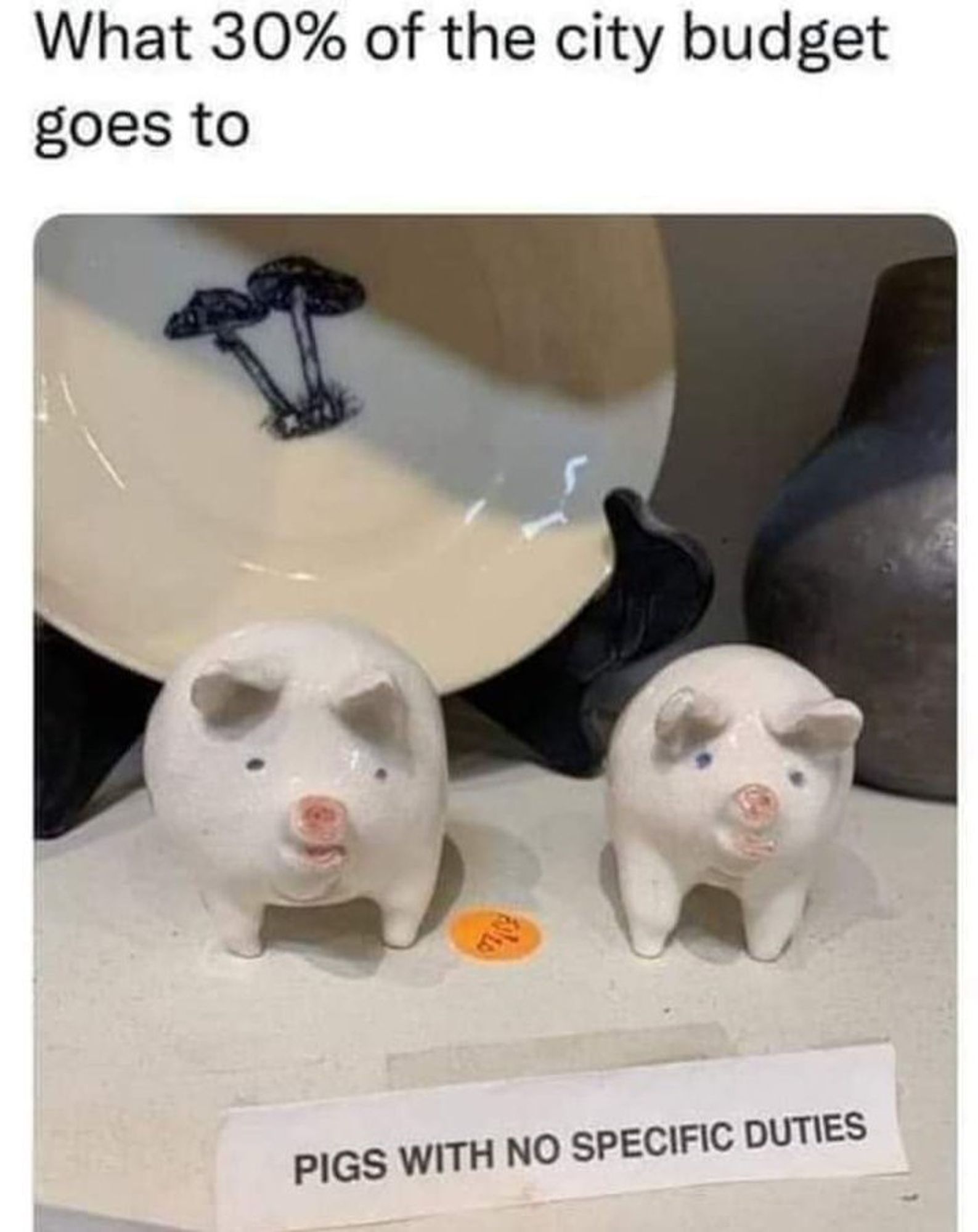 An image of two small white porcelain pigs sitting on a plate. A paper sign says "Pigs with no specific duties". The caption reads "What 30% of the city budget goes to"