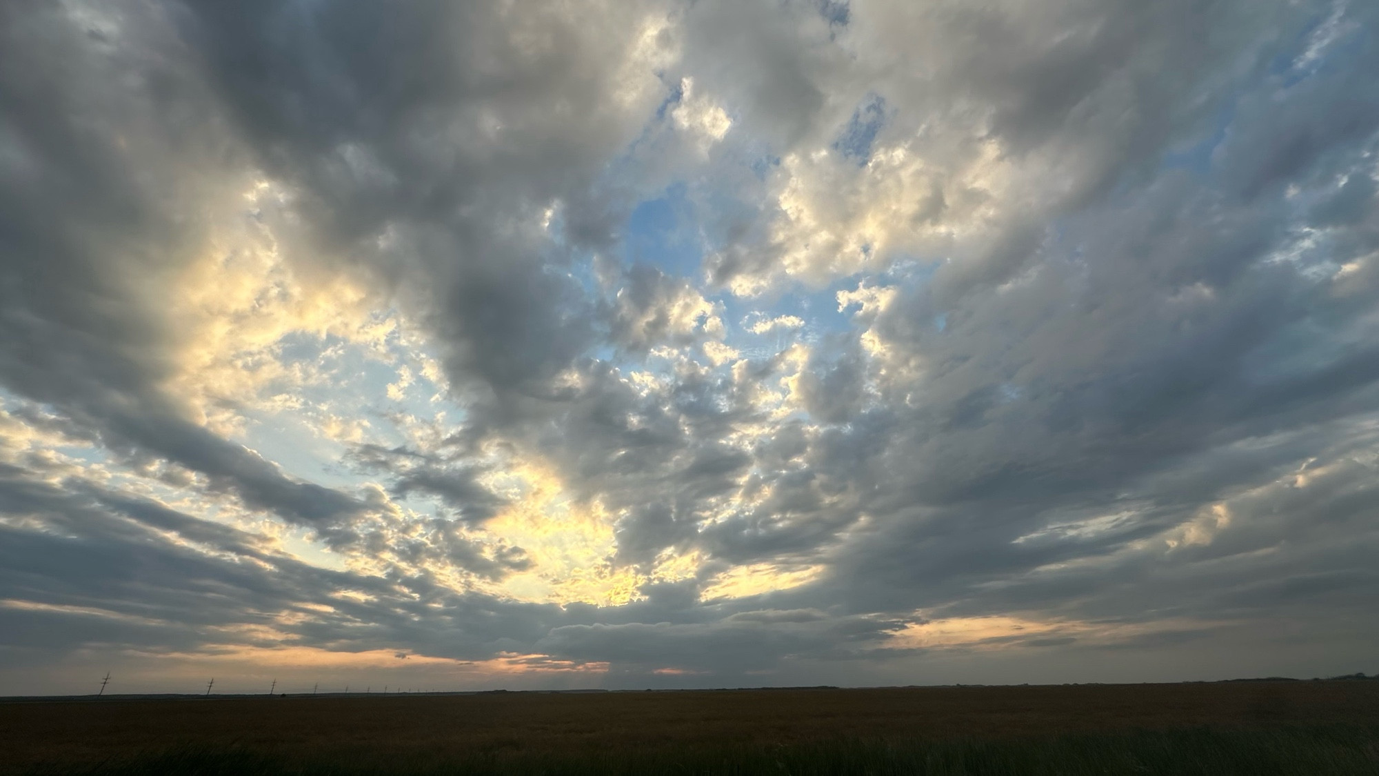 A dramatic sky filled with golden-fringed clouds sweeps over a wide open field of brown grasses.