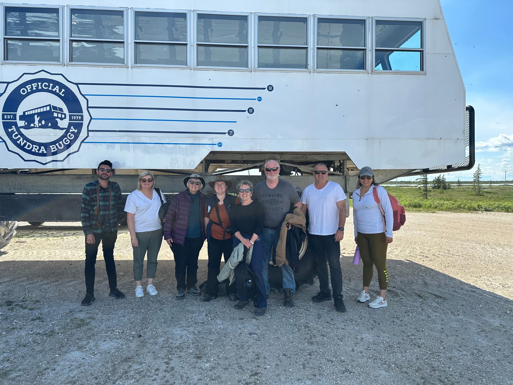 A group of people stand in front of an enormous white all-terrain vehicle known as the tundra buggy. They are only as tall as the wheels of the machine.