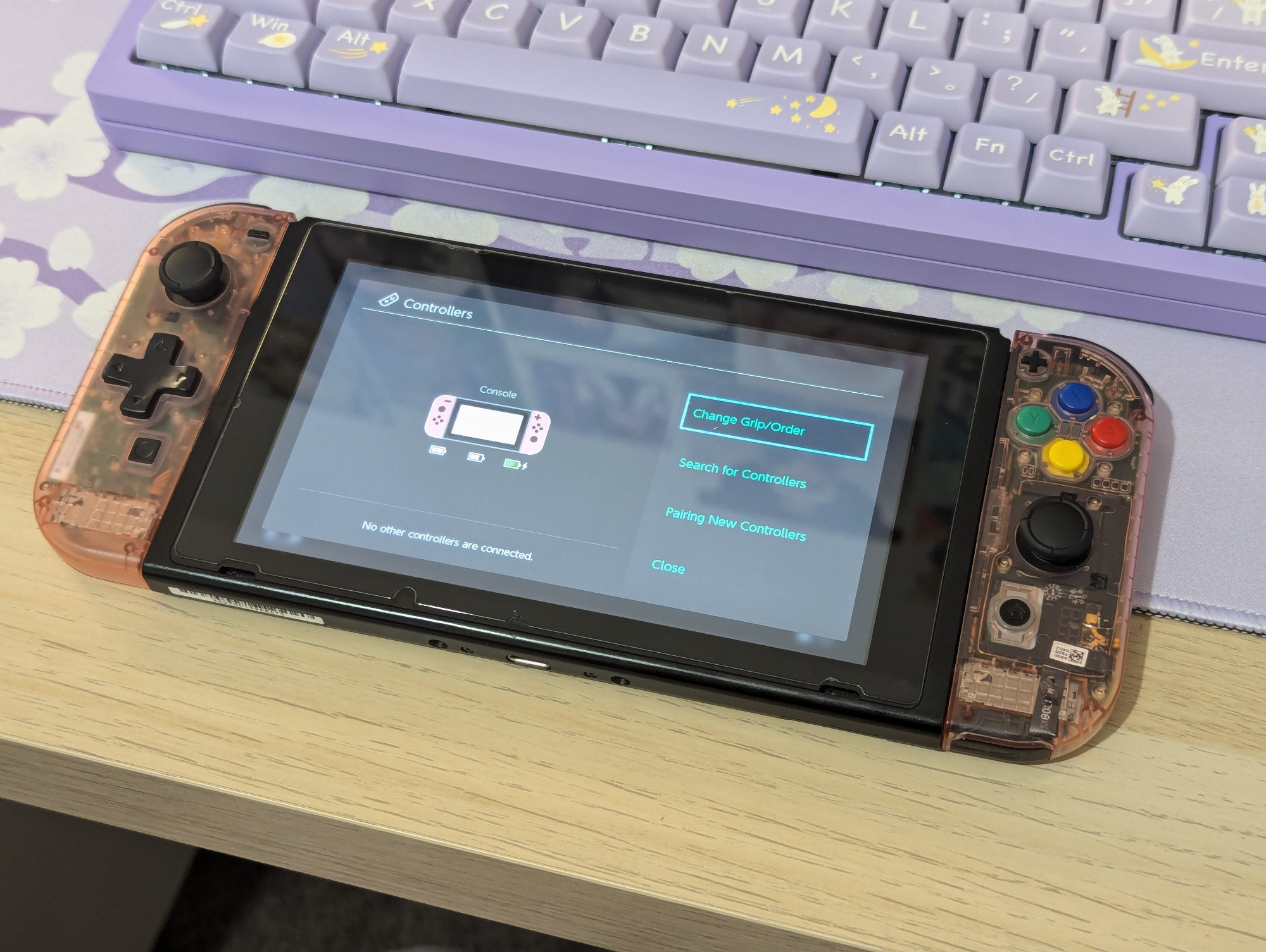 A Nintendo switch console laid on a light wood bench with joycons in transparent pink shells, a dpad mod and SNES style coloured ABXY buttons