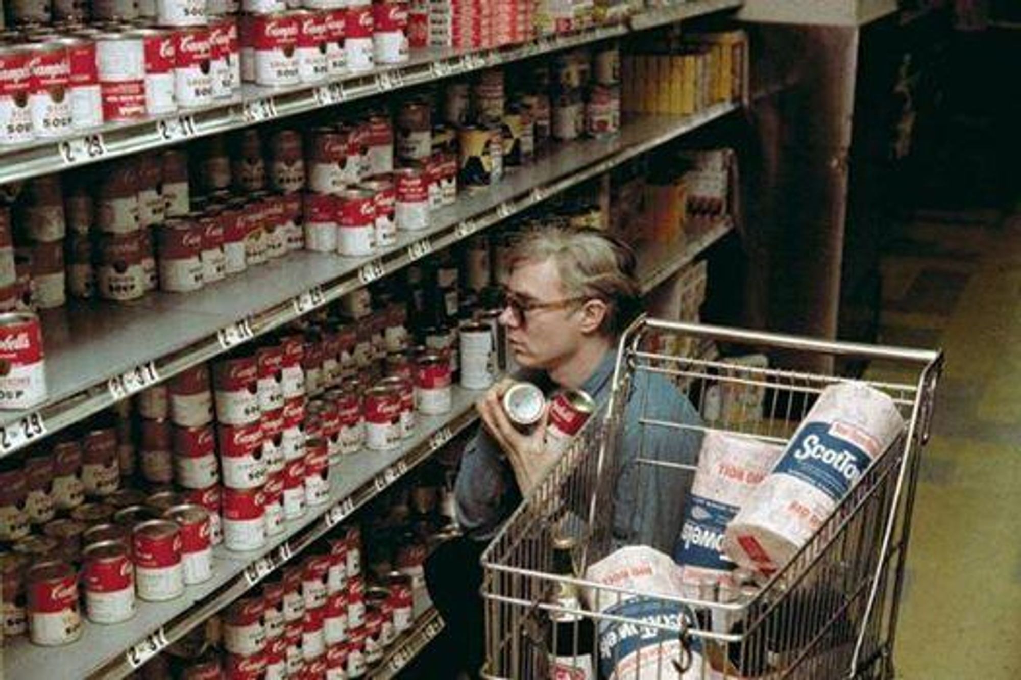 photo of Andy Warhol shopping at supermarket, with shopping cart full of paper towels and arms full of Campells Soup™ cans