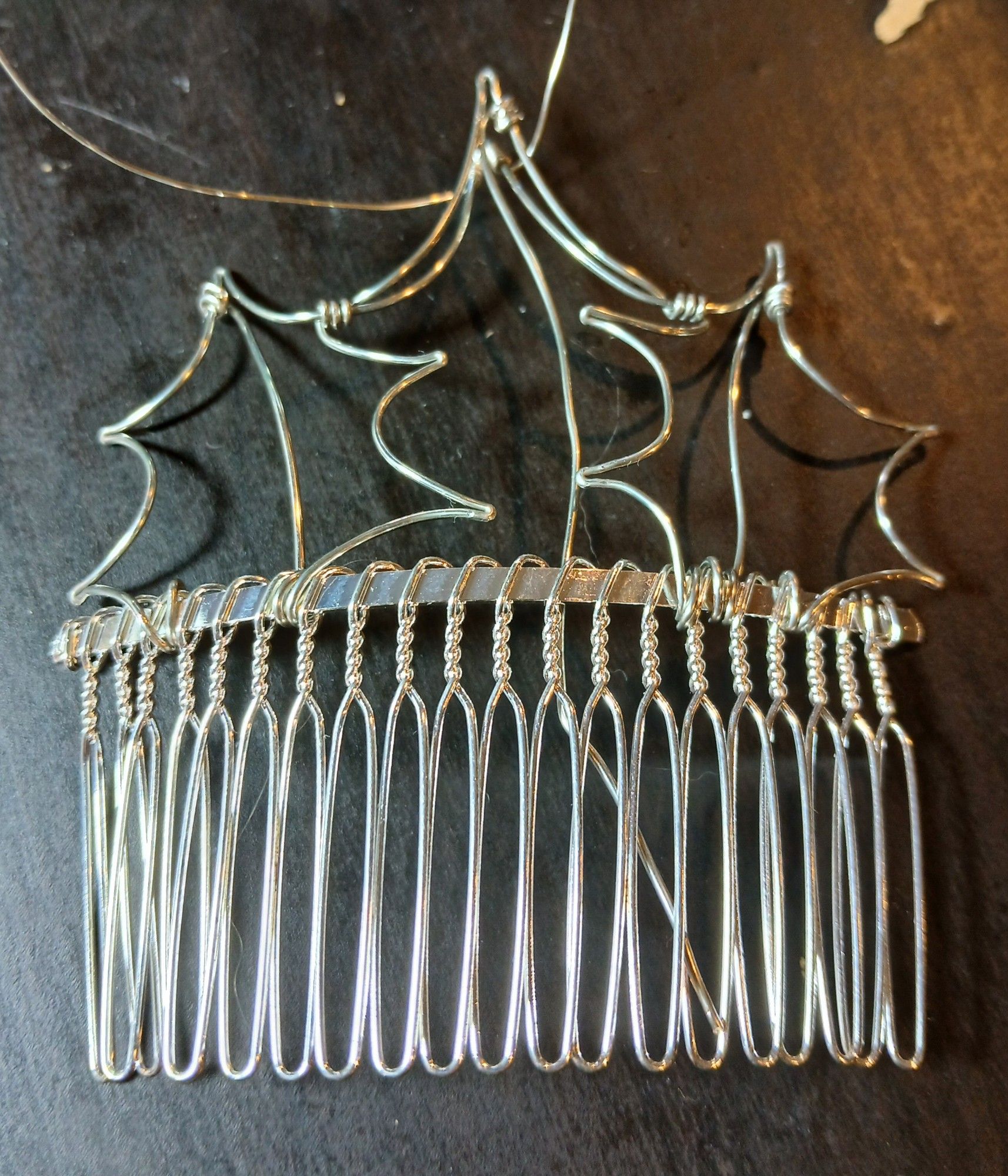 A silver metal hair comb, with a wire frame attached to the top. The frame is silver wire, shaped and bent into outlines of pointy leaves. It's still bare but ready for beading.