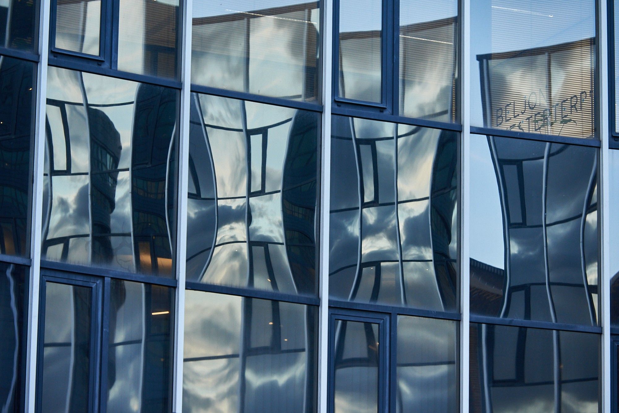 A shot of a wall made of glass panes with straight lines but all the reflections of other glass pane are very crooked.