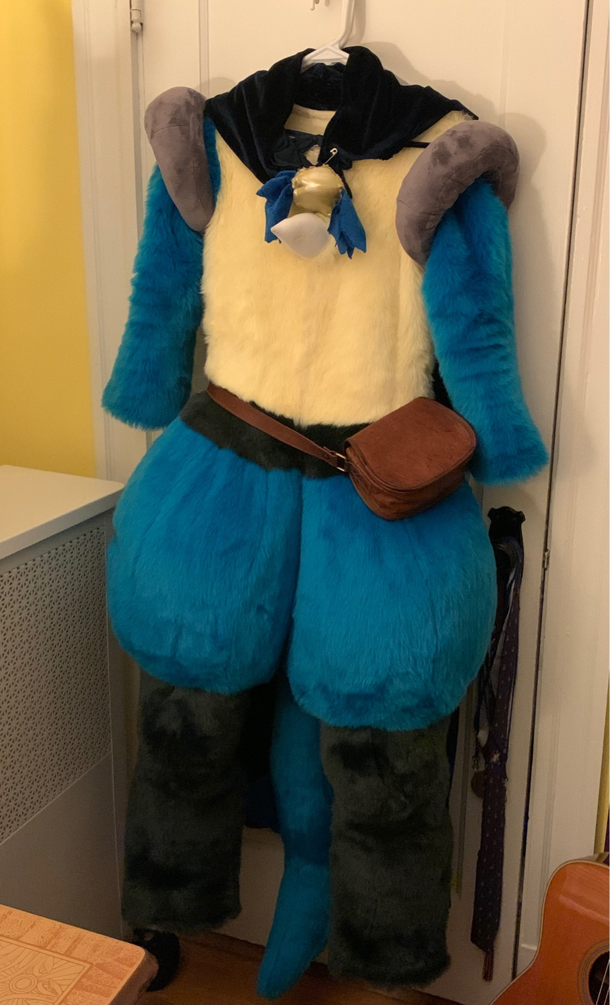 A Lucario fursuit wearing a navy blue cape and a brown leather satchel