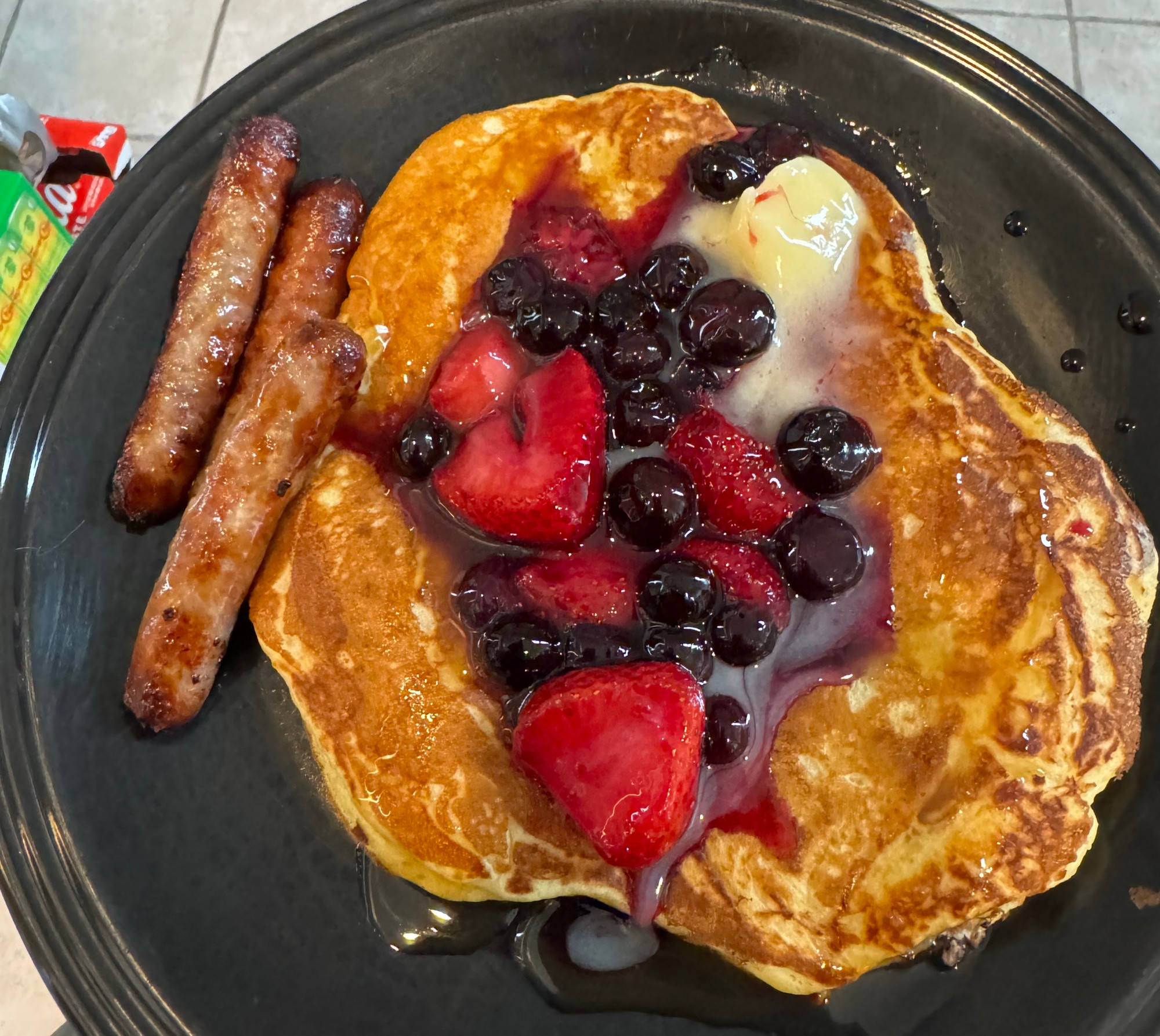 A plate with pancakes, sausage, and a berry compote.