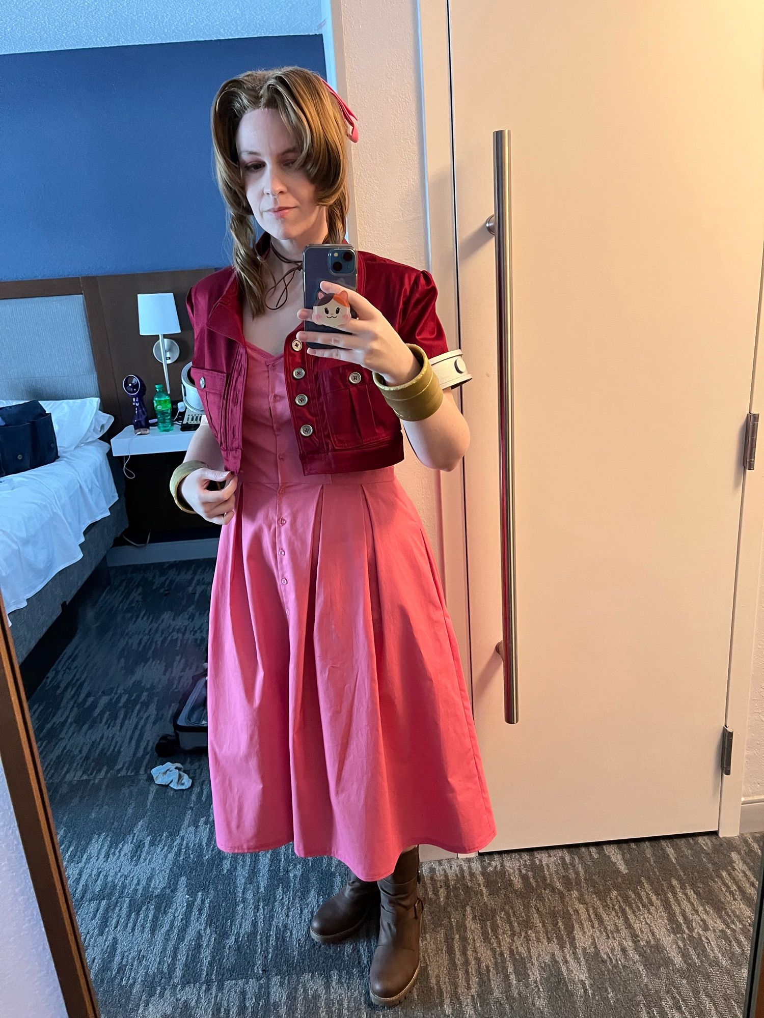 Fem person dressed as Aerith from Final Fantasy VII taking a selfie in a hotel room mirror