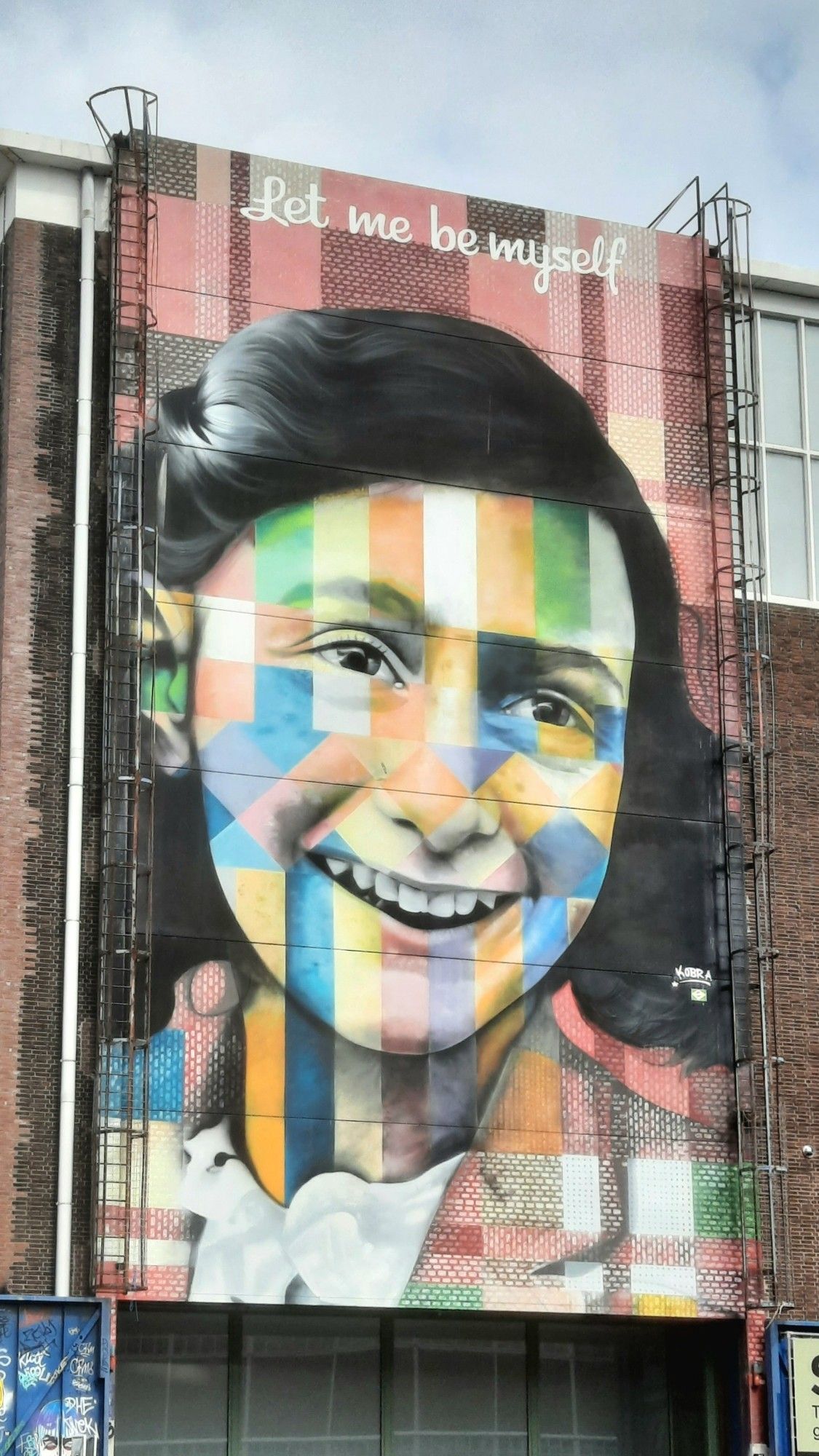 Ein riesiges Porträt von Anne Frank, circa 5 mal 8 Meter. Sie lächelt in Regenbogenfarben.