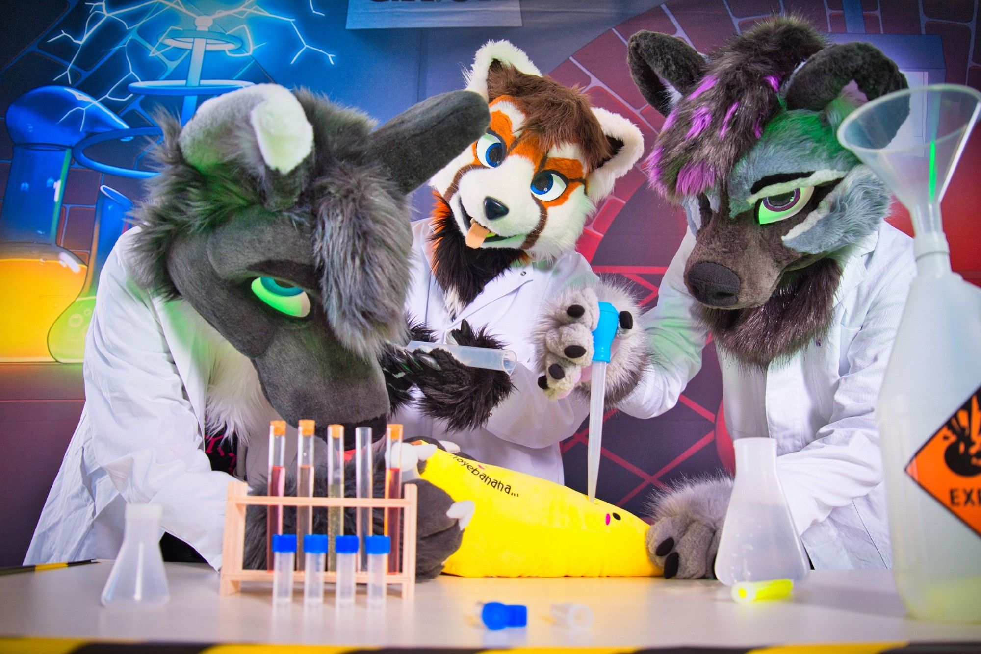 Three fursuiters in labcoats posing with fake lab equipment, appearing to do experiments with a plush banana.