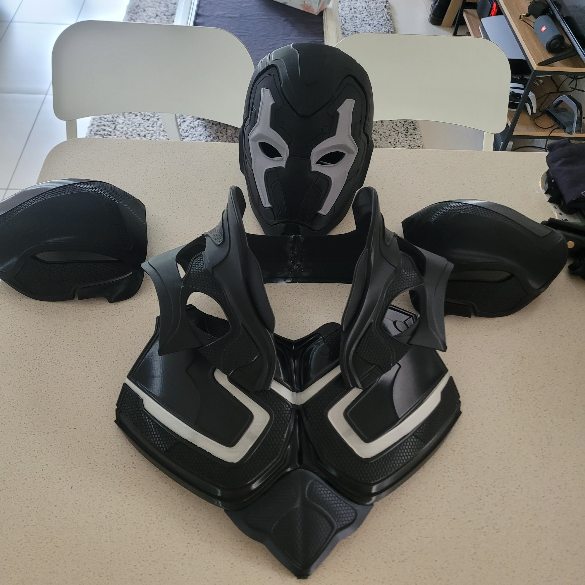 A picture of a half assembled blue beetle costume, that I sitting on a kitchen bench. Printed up in a black plastic filament.