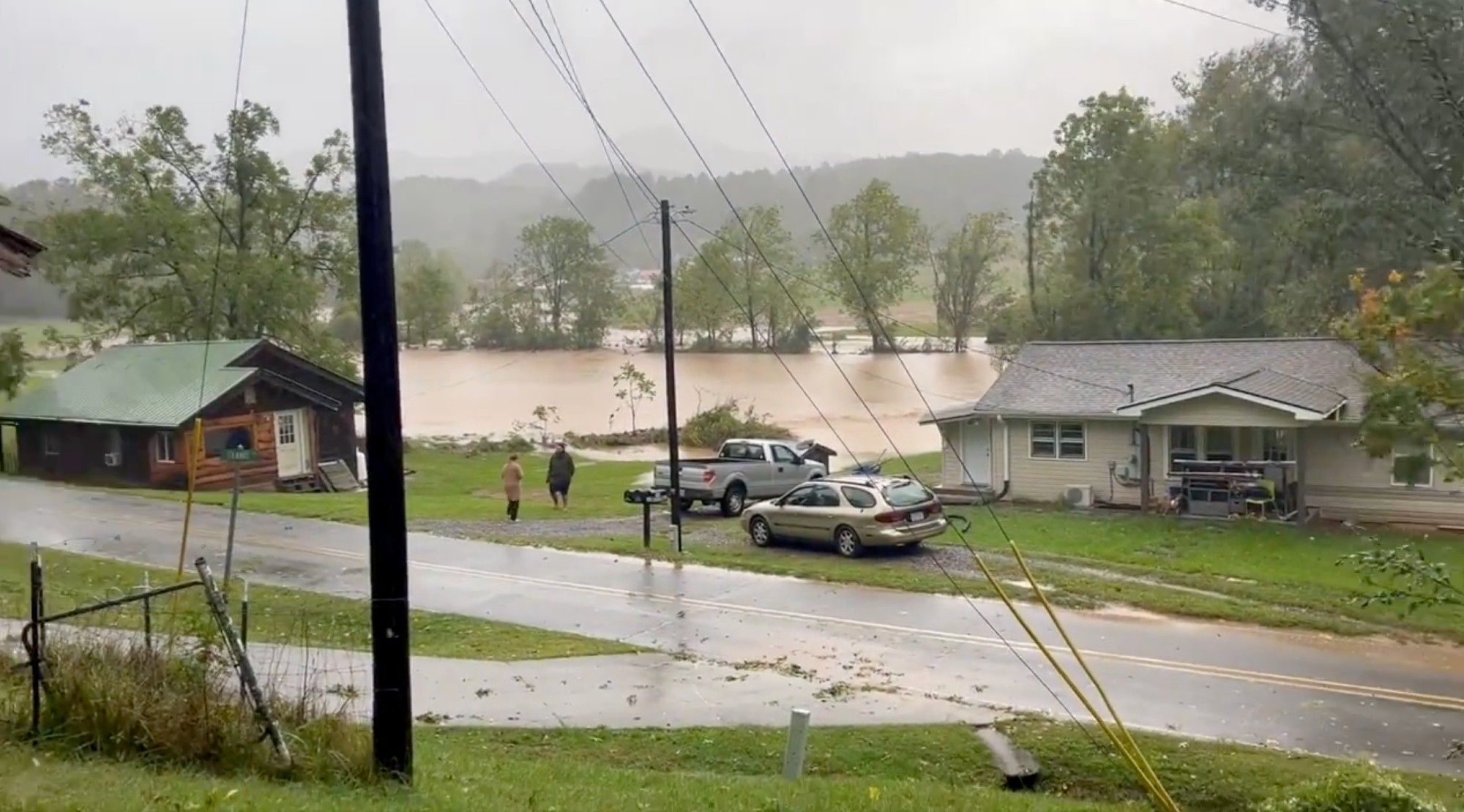 a wet road on the other side of which is a large field flooded with flowing muddy water